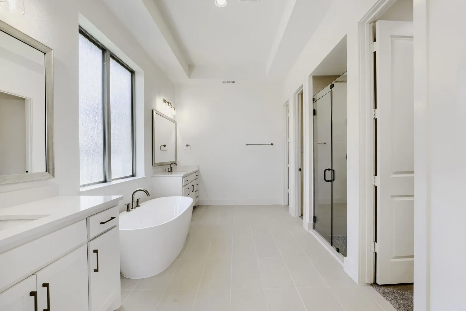 Dual vanity with stone countertops, freestanding soaking tub, and a glass-enclosed shower