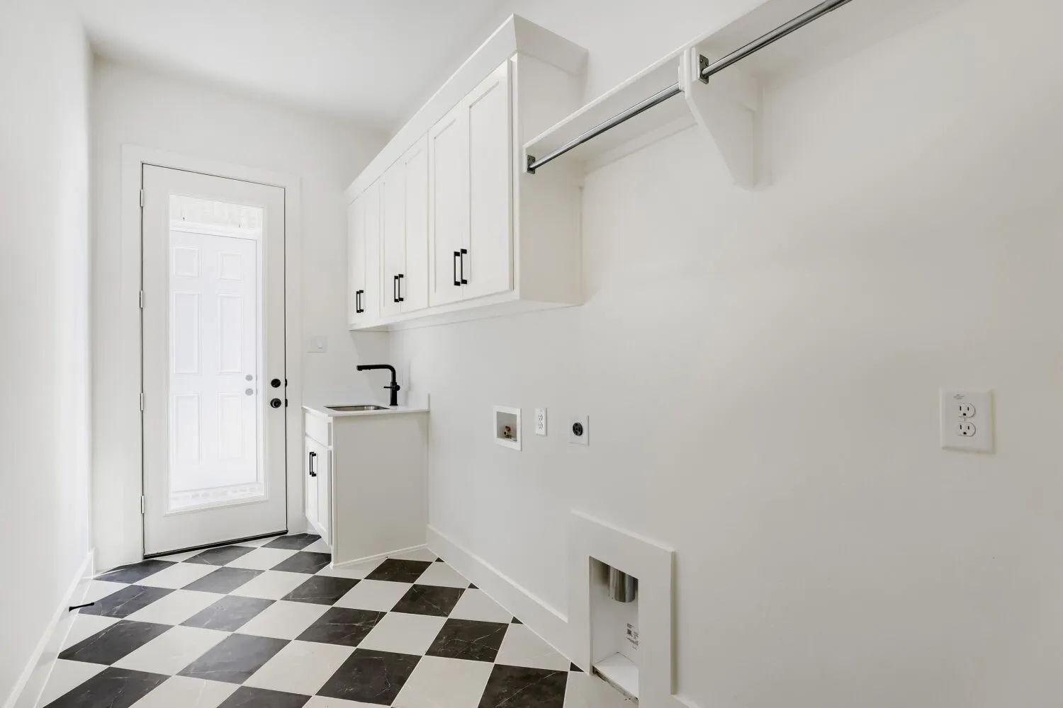 White shaker-style cabinetry with matte black hardware, utility sink with a black gooseneck faucet, black and white checkered flooring, and a glass-paneled exterior door
