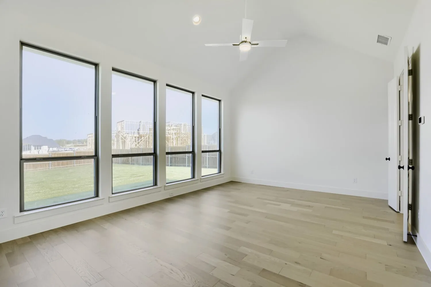 Vaulted ceiling with a ceiling fan, light wood-finish flooring, and multiple floor-to-ceiling windows