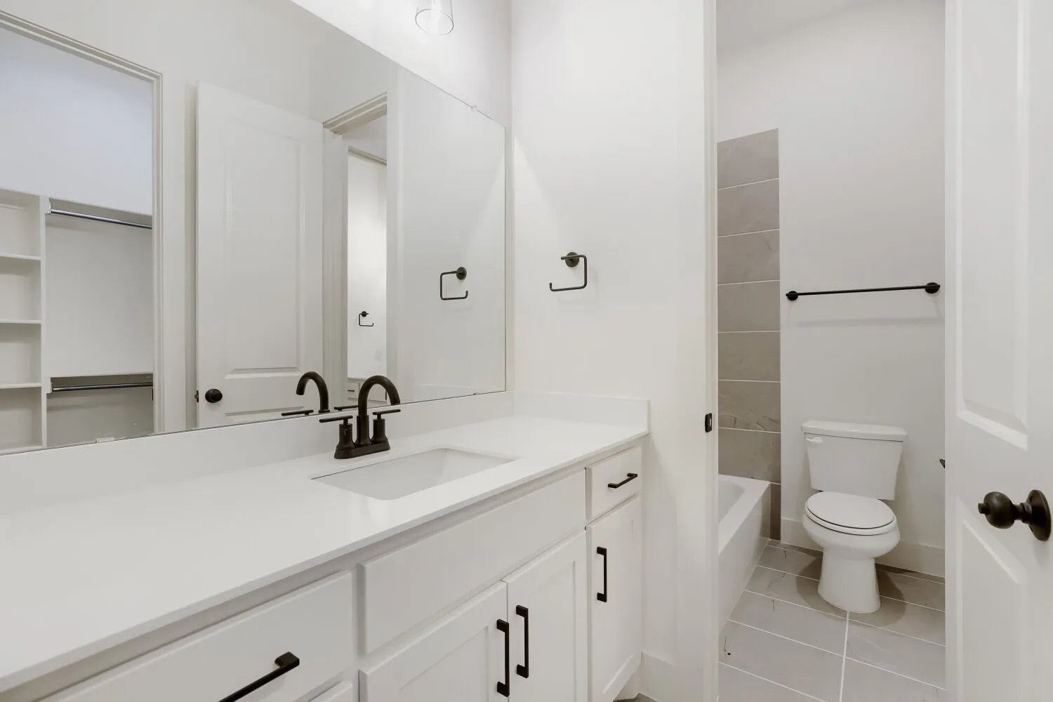 White vanity with an integrated sink, dark bronze hardware, a full-width mirror, and a built-in closet with shelving