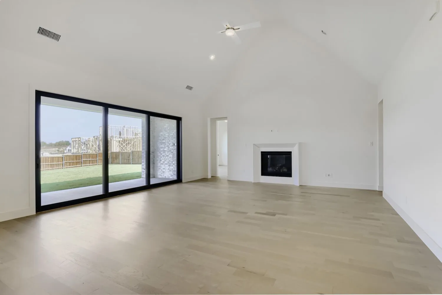 Vaulted ceiling with a ceiling fan, fireplace with a white surround, and wood-finish flooring