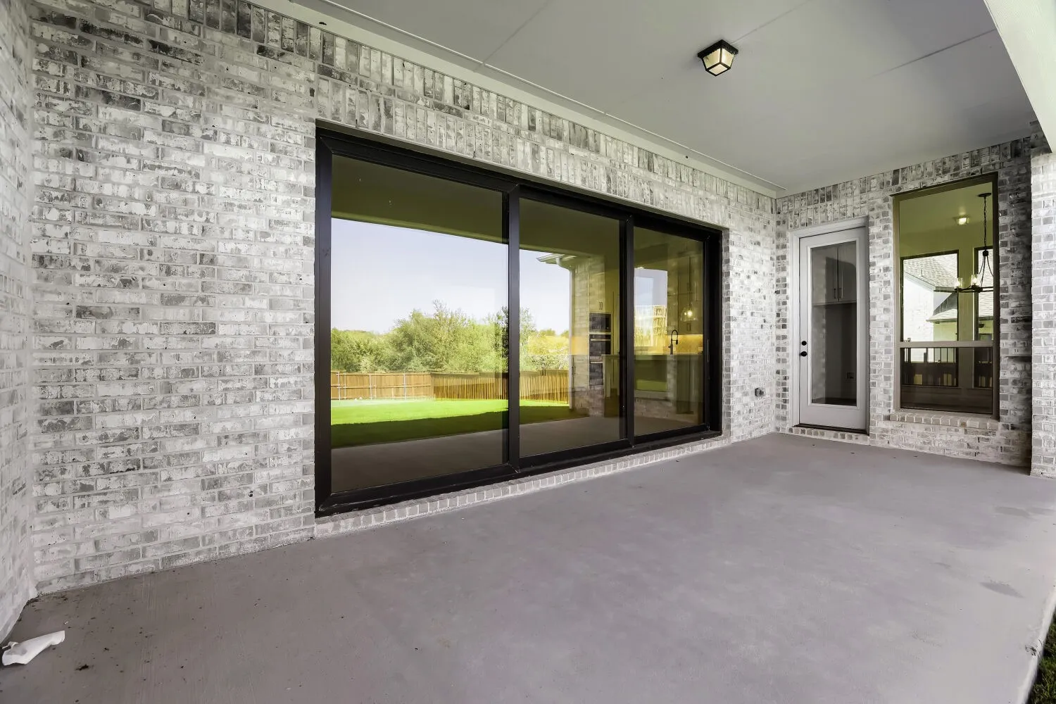 Covered patio featuring a concrete surface, white brick exterior, black frame sliding glass door, and recessed lighting