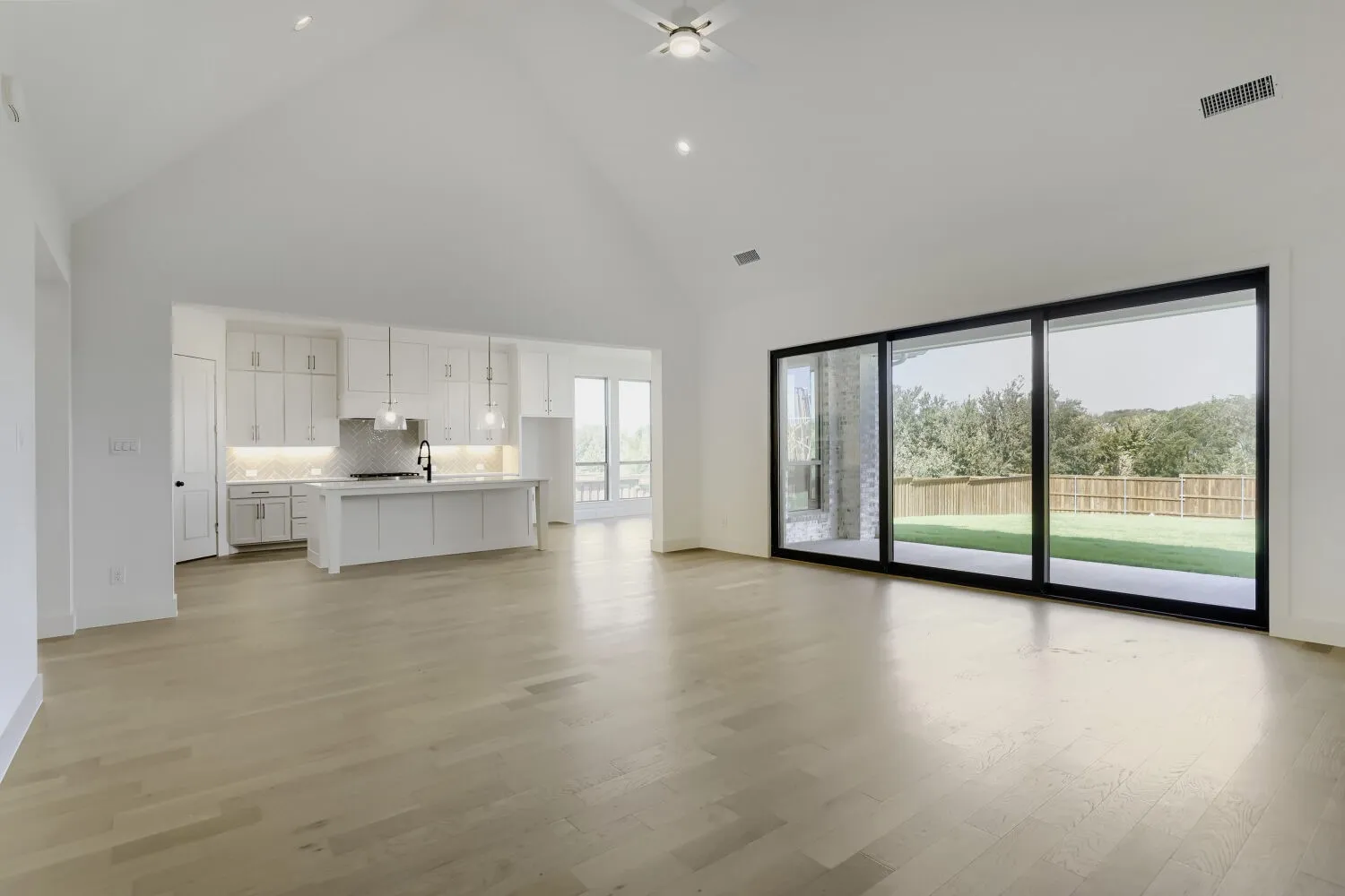 Vaulted ceiling, wood-finish flooring, white cabinetry, kitchen island with pendant lighting, and large sliding glass doors