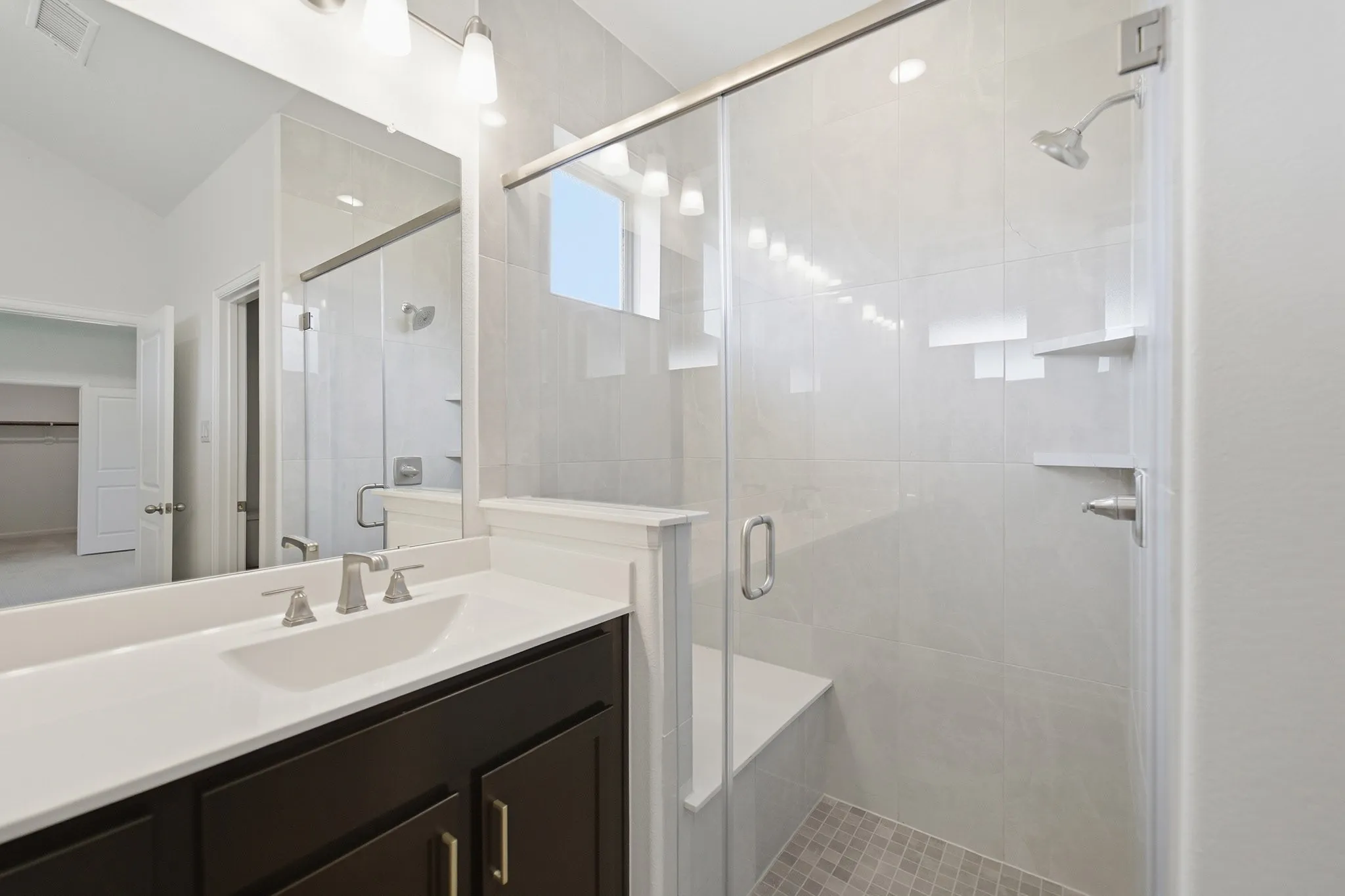 Glass-enclosed shower with a built-in bench and shelves, subway tile surround, and mosaic tile flooring