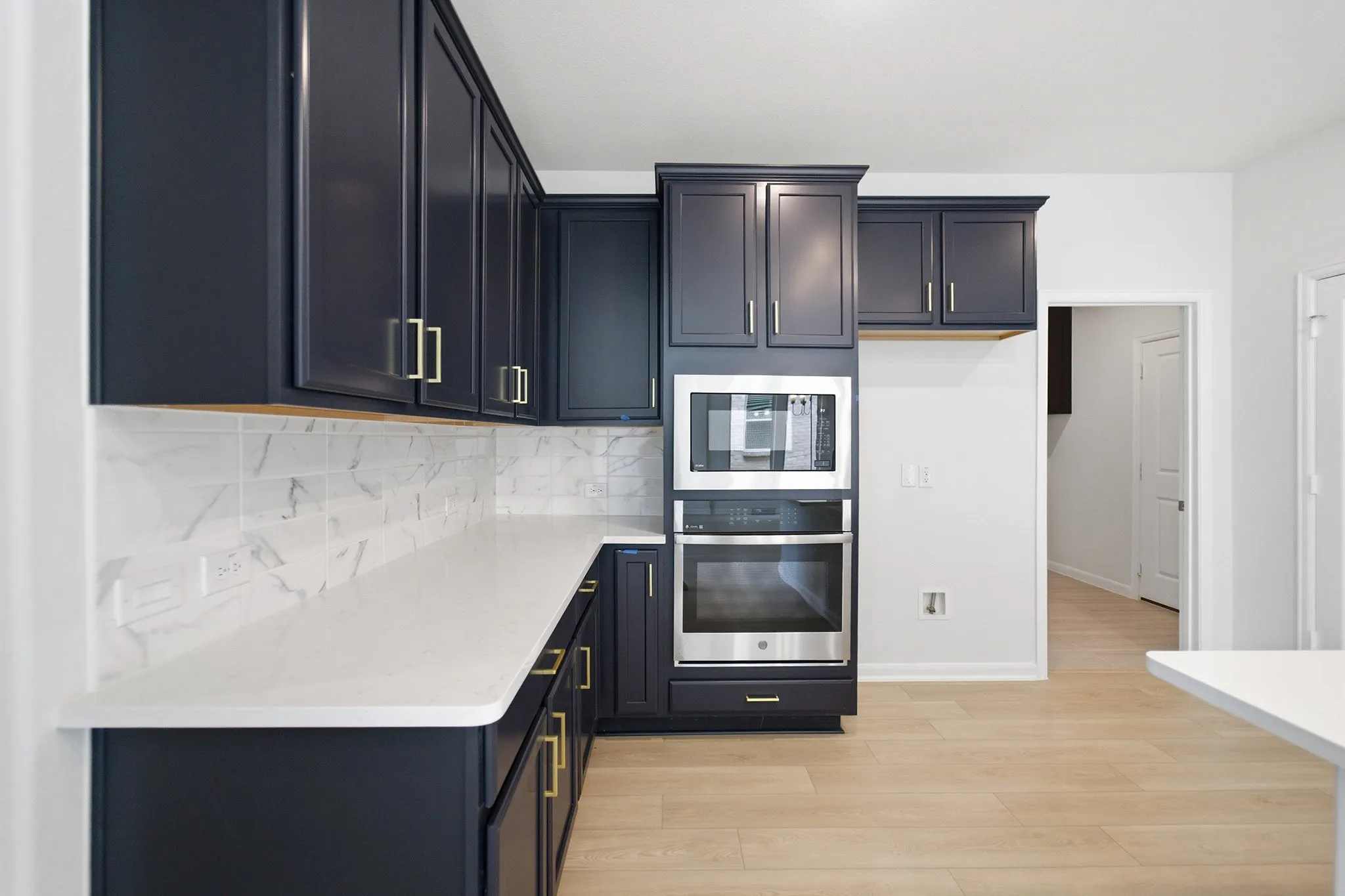 Kitchen featuring dark cabinetry with gold-finish hardware, white countertops, tile backsplash, built-in stainless steel microwave, and built-in stainless steel oven