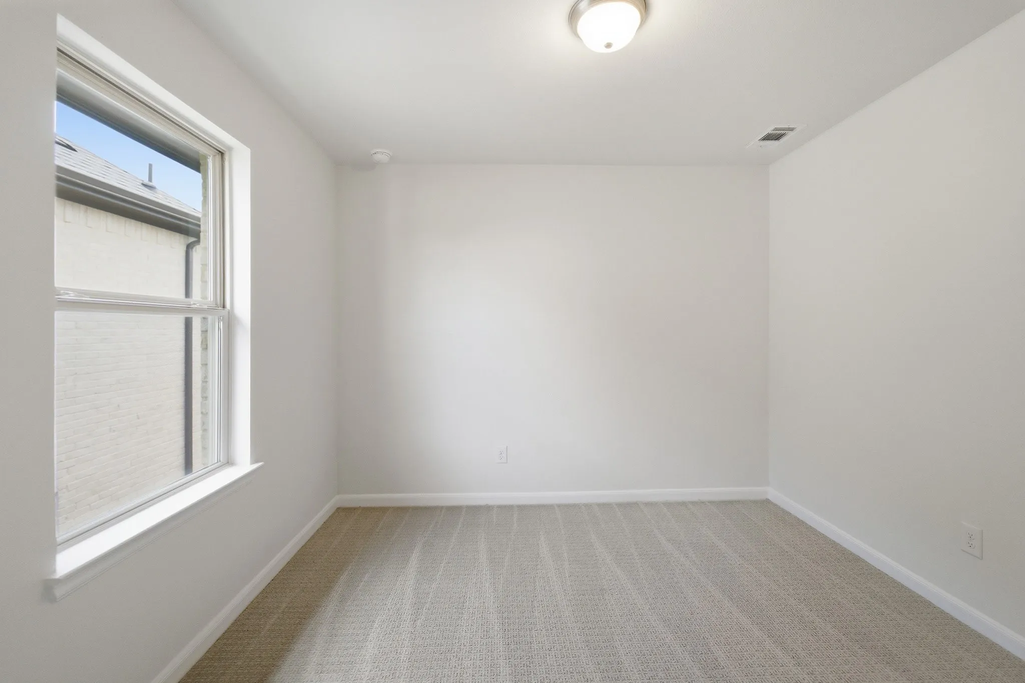 Spacious room featuring neutral carpeting, white painted walls, a single window with white trim, and a ceiling-mounted light fixture