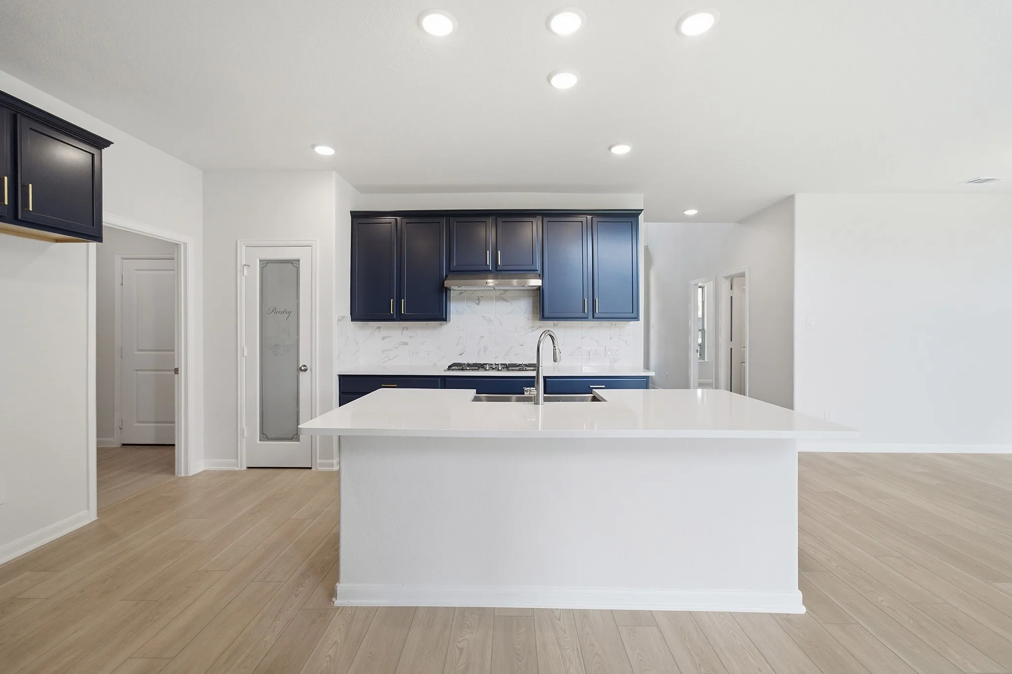 Open-concept kitchen featuring a large island with an undermount sink, dark blue cabinetry, white countertops, and wood-finish flooring