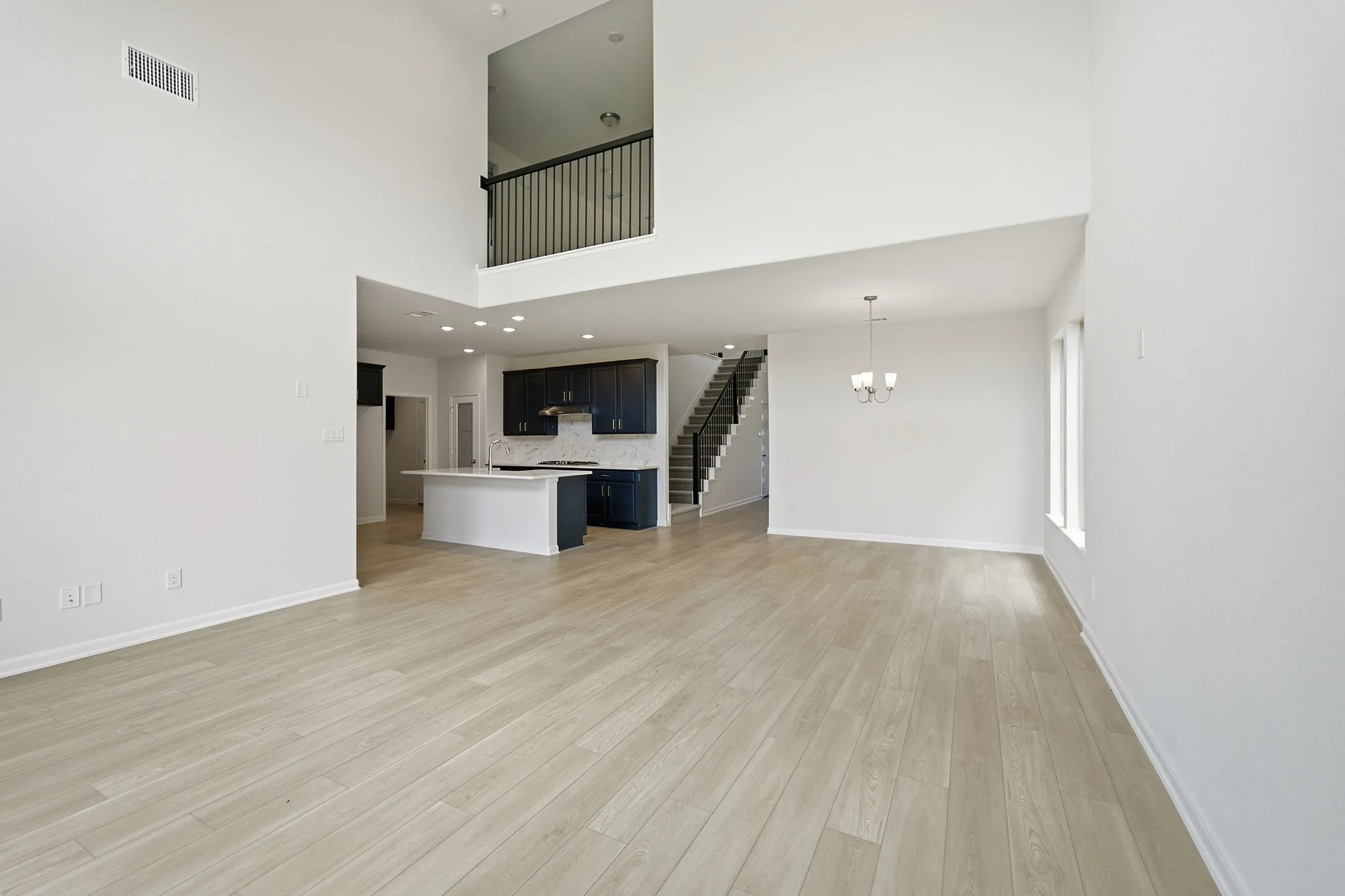 Open-concept main living area featuring high ceilings, light wood-finish flooring, and a contemporary chandelier