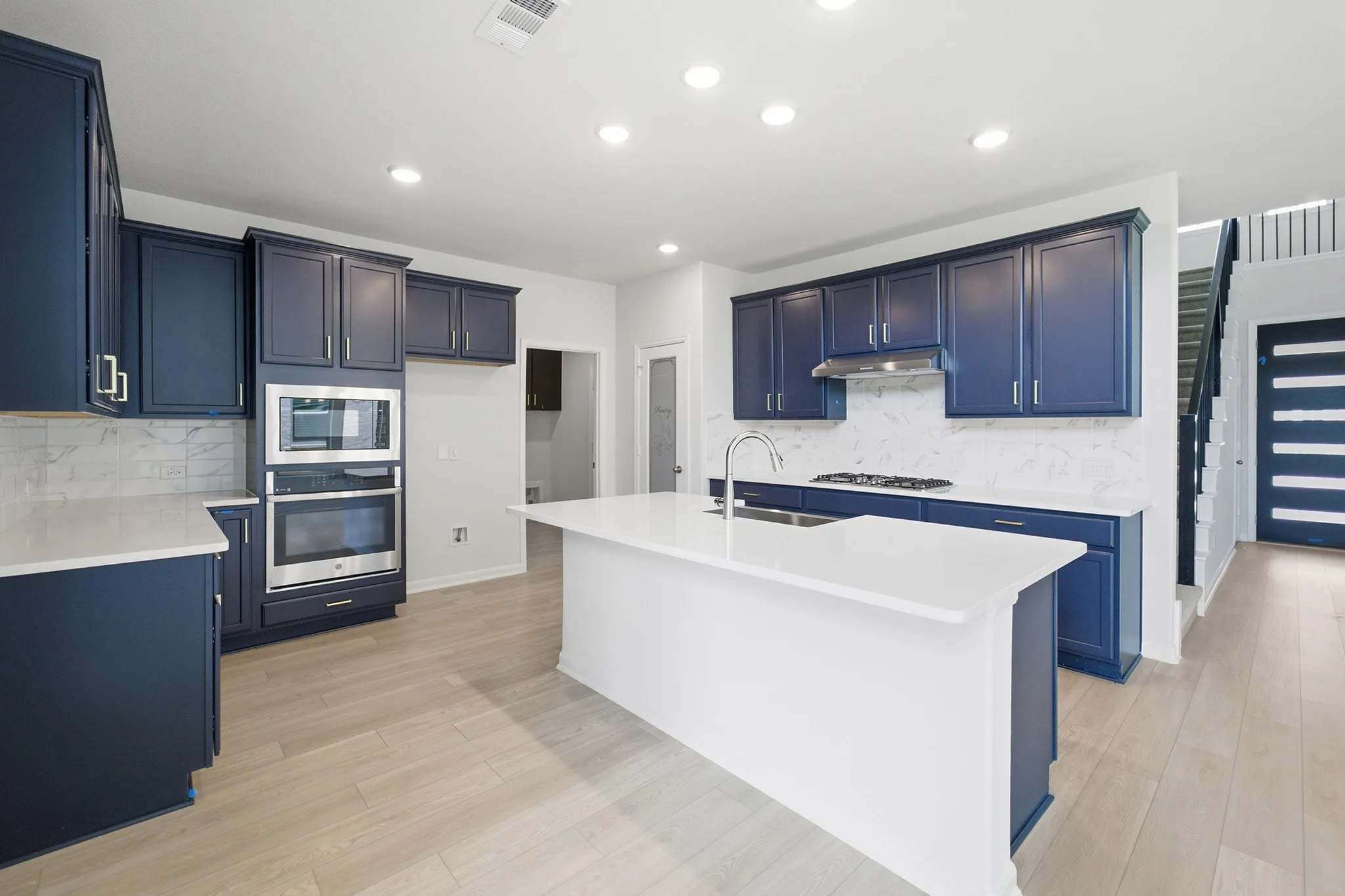 Modern kitchen featuring navy cabinetry, a substantial island with a basin sink, light wood-finish flooring, and recessed lighting