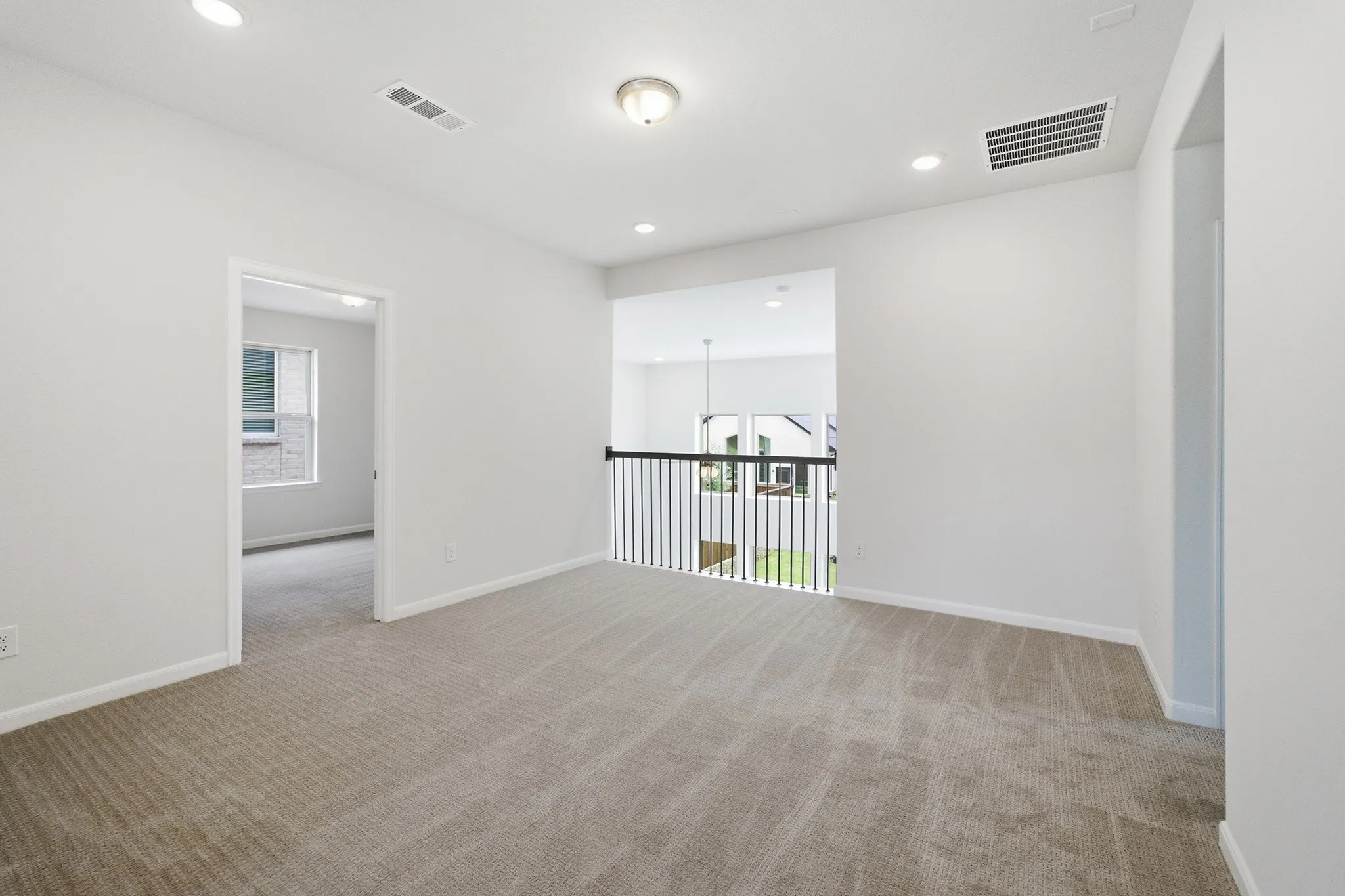 Carpeted landing area featuring a black metal railing overlooking a lower level, recessed ceiling lighting, and a single ceiling-mounted light fixture