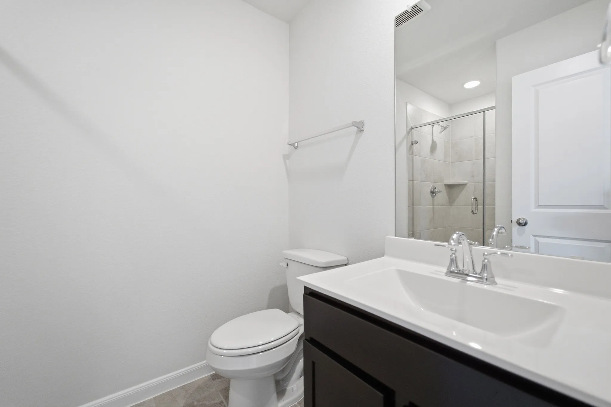 Bathroom featuring a dark wood-finish vanity with an integrated sink, polished chrome fixtures, a frameless mirror, and a glass-enclosed shower with tiled walls
