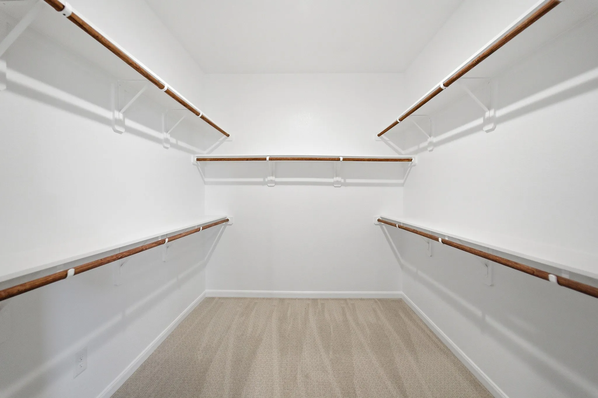 Walk-in closet featuring light beige carpeting, white walls, multiple built-in shelving units, and wood-finish hanging rods