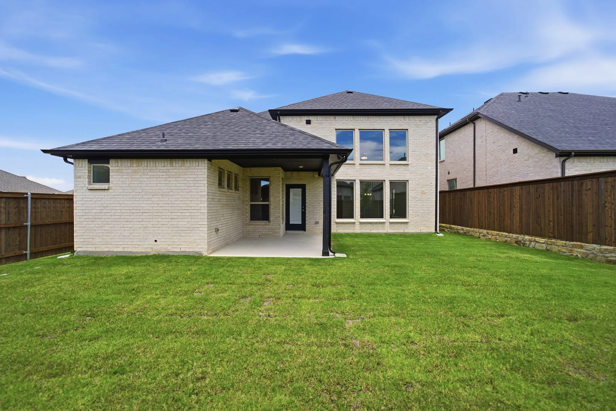 Spacious backyard featuring an extended concrete patio, full privacy fencing, and a light brick exterior