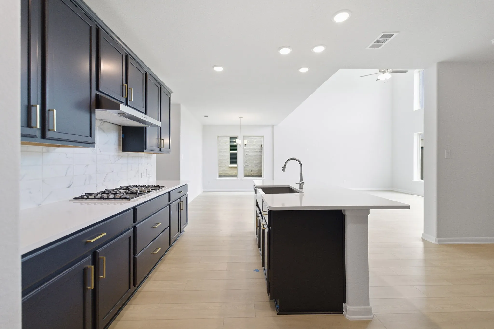 Modern kitchen featuring dark cabinetry with gold-tone hardware, white countertops, and a subway tile backsplash