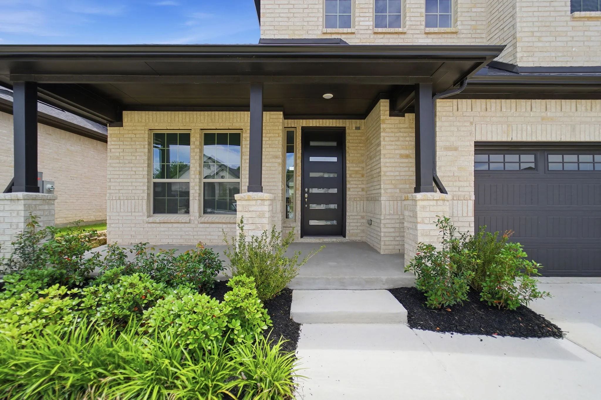 Cream brick facade with a dark trim portico, featuring a modern black entry door with horizontal lites