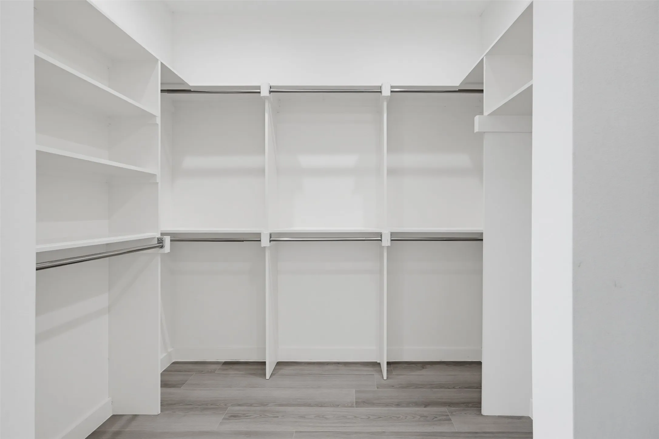 Walk-in closet featuring built-in white shelving, multiple hanging rods, and wood-finish flooring