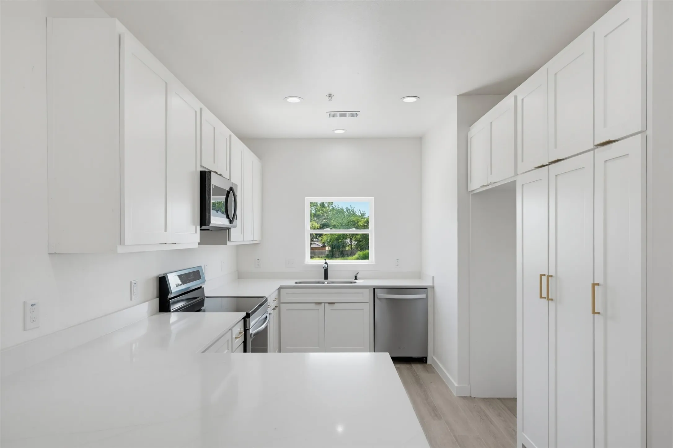Modern kitchen featuring white shaker cabinetry, stainless steel appliances, light-toned countertops, a built-in microwave, and wood-finish flooring