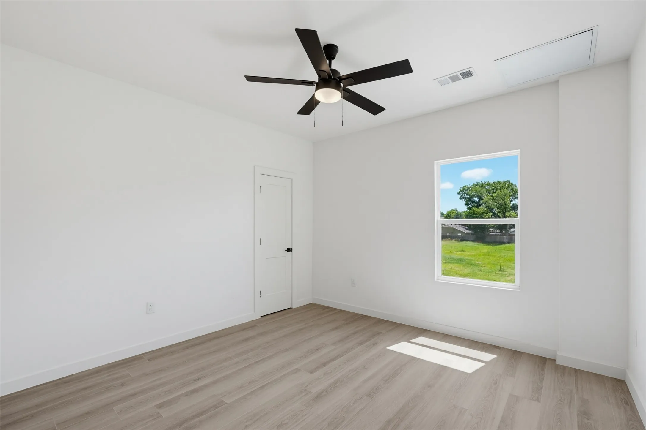 Room featuring wood-finish flooring, a contemporary ceiling fan with integrated lighting, white walls, and a white interior door
