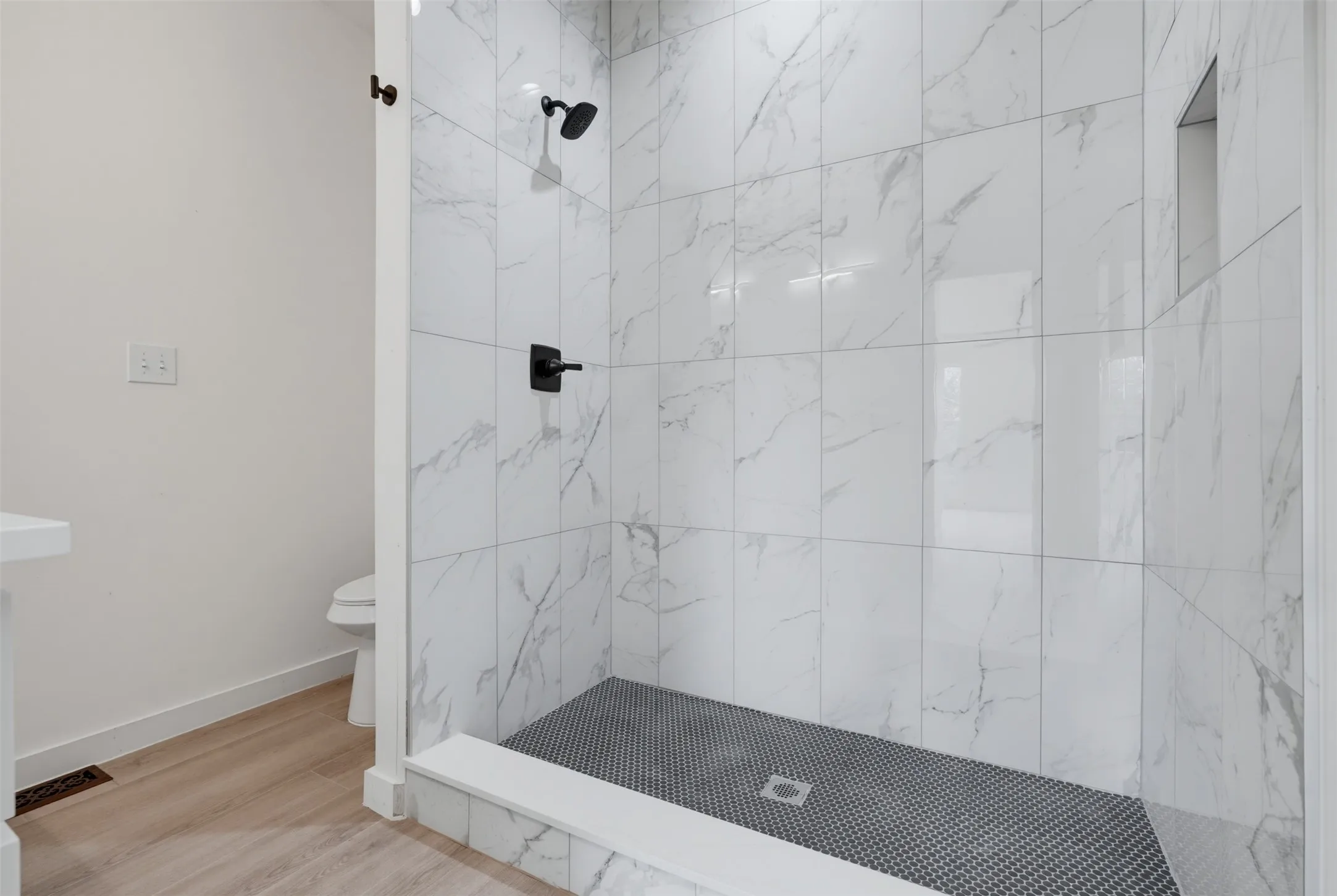 Walk-in shower featuring white marble-look subway tile, a dark penny tile floor, a built-in shower niche, and matte black fixtures