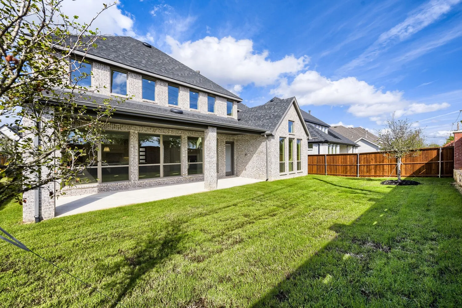 Expansive grassy yard with a wood fence, covered patio, and large windows