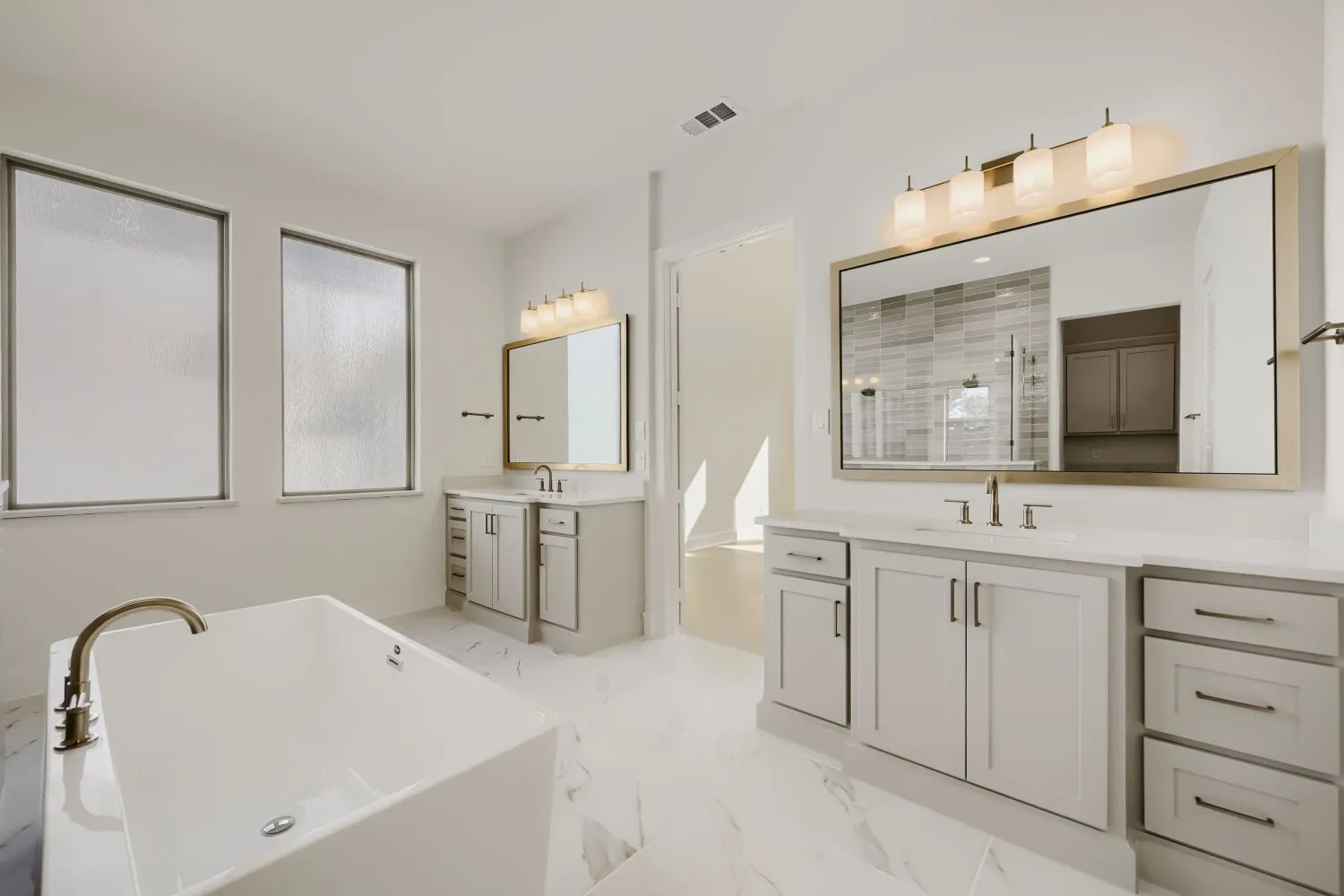 Freestanding soaking tub with a floor-mounted faucet, dual vanities with integrated sinks, large framed mirrors, and contemporary light fixtures