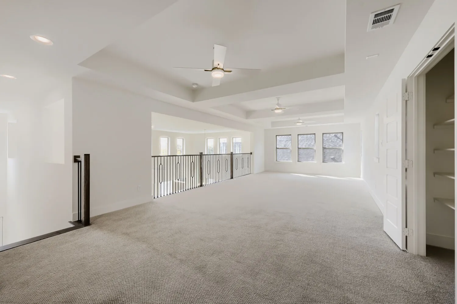 Spacious carpeted room featuring tray ceilings, recessed lighting, ceiling fans, and multiple windows