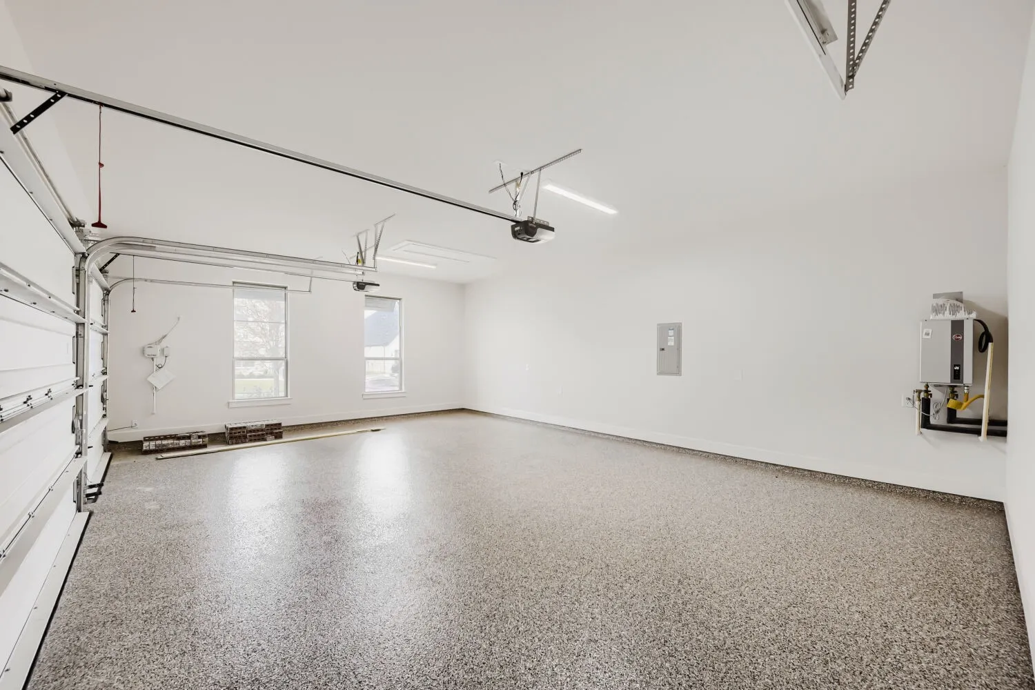 Large garage space featuring a speckled epoxy floor, two windows with blinds, and white walls