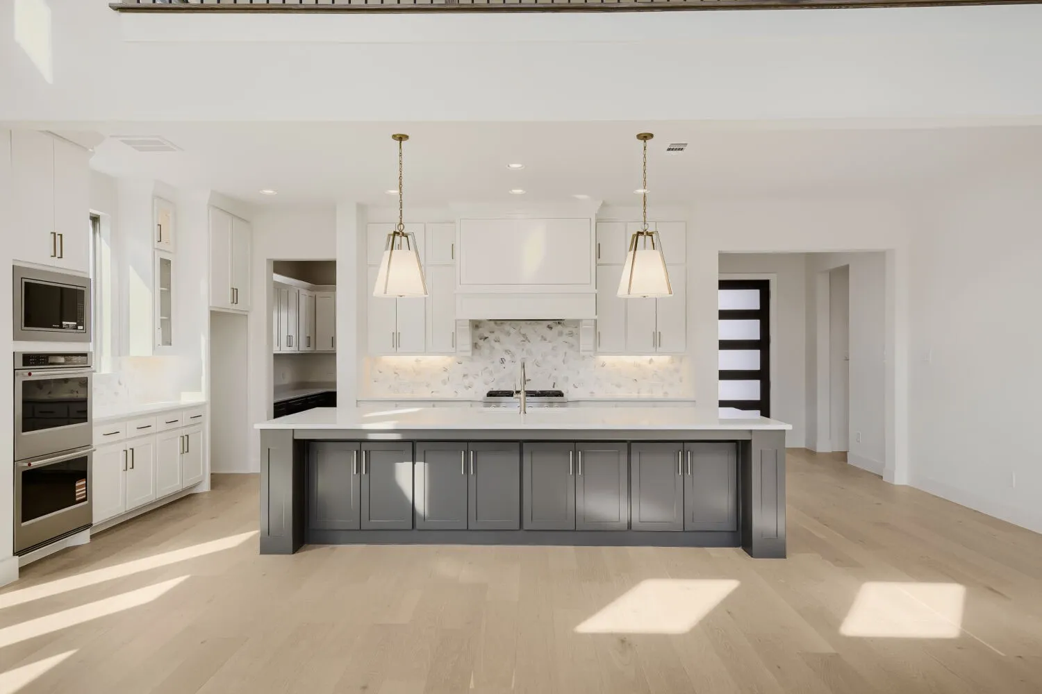 Kitchen featuring a large island with gray cabinetry, white perimeter cabinetry, stainless steel double ovens, and wood-finish flooring