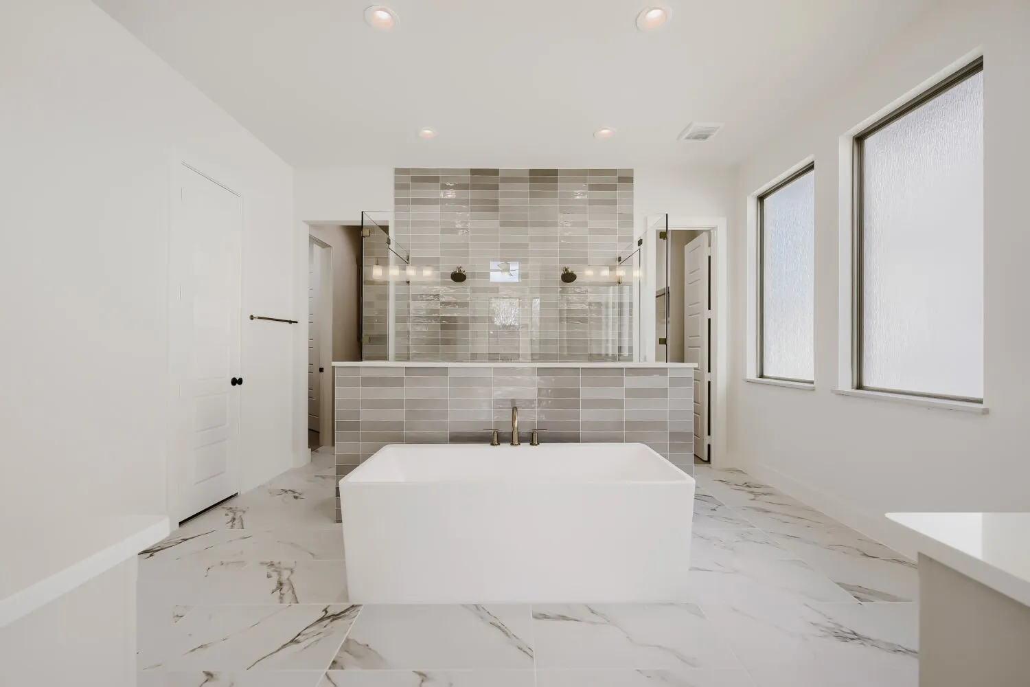 Freestanding soaking tub with floor-mounted faucet, marble-look tile flooring, and a tiled shower enclosure with glass panels