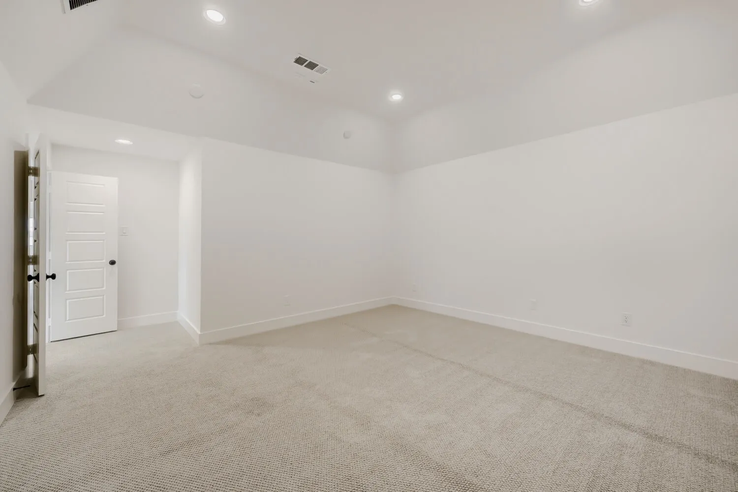 Recessed lighting illuminates the carpeted flooring and crisp white walls, complemented by a white paneled door with black hardware