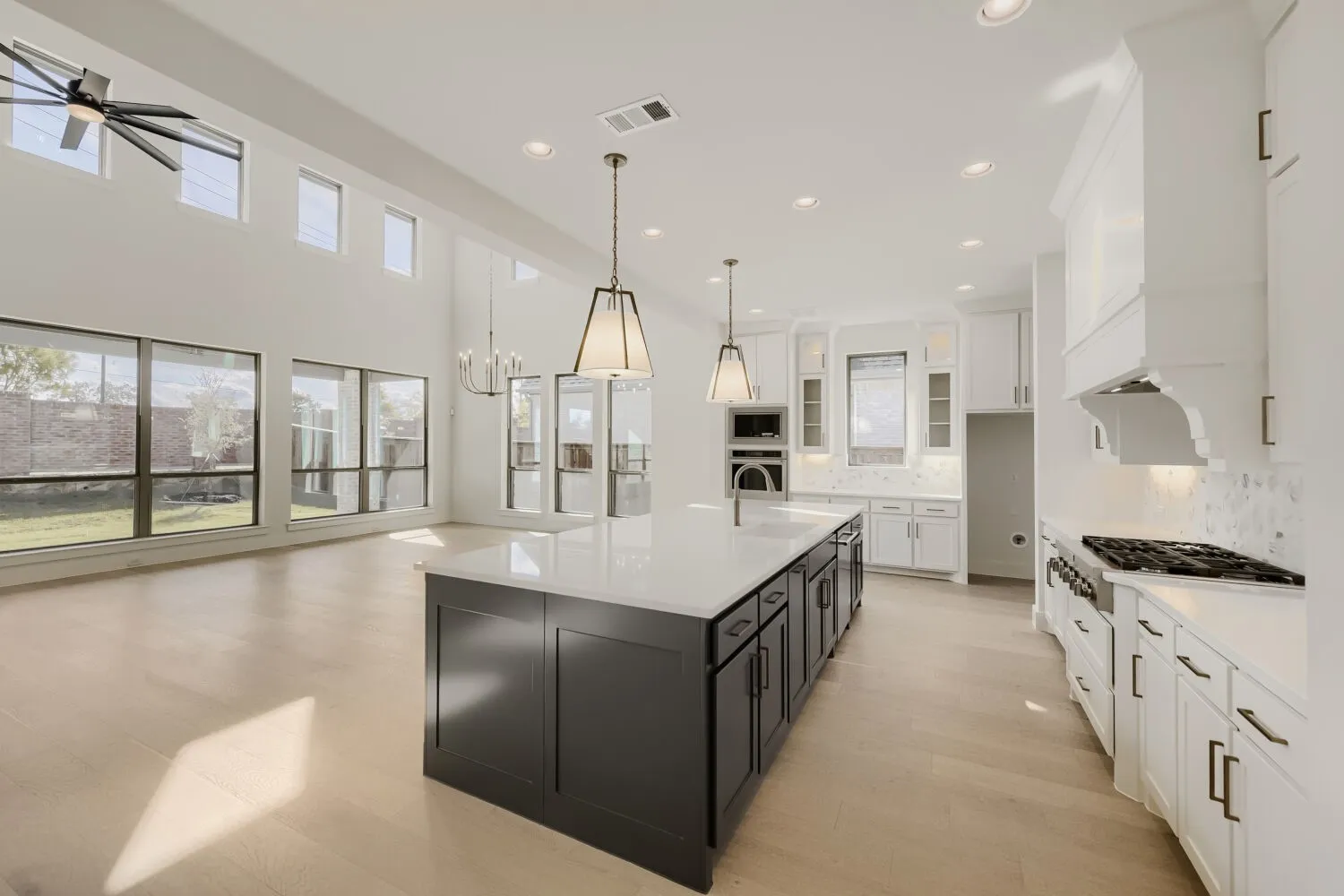 Spacious open-concept layout featuring high ceilings, wood-finish flooring, a contemporary kitchen island with a built-in sink, and extensive recessed lighting