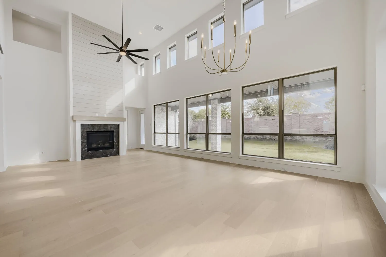 Expansive living space featuring wood-finish flooring, a fireplace with a dark stone surround and shiplap accent wall, and multiple large windows