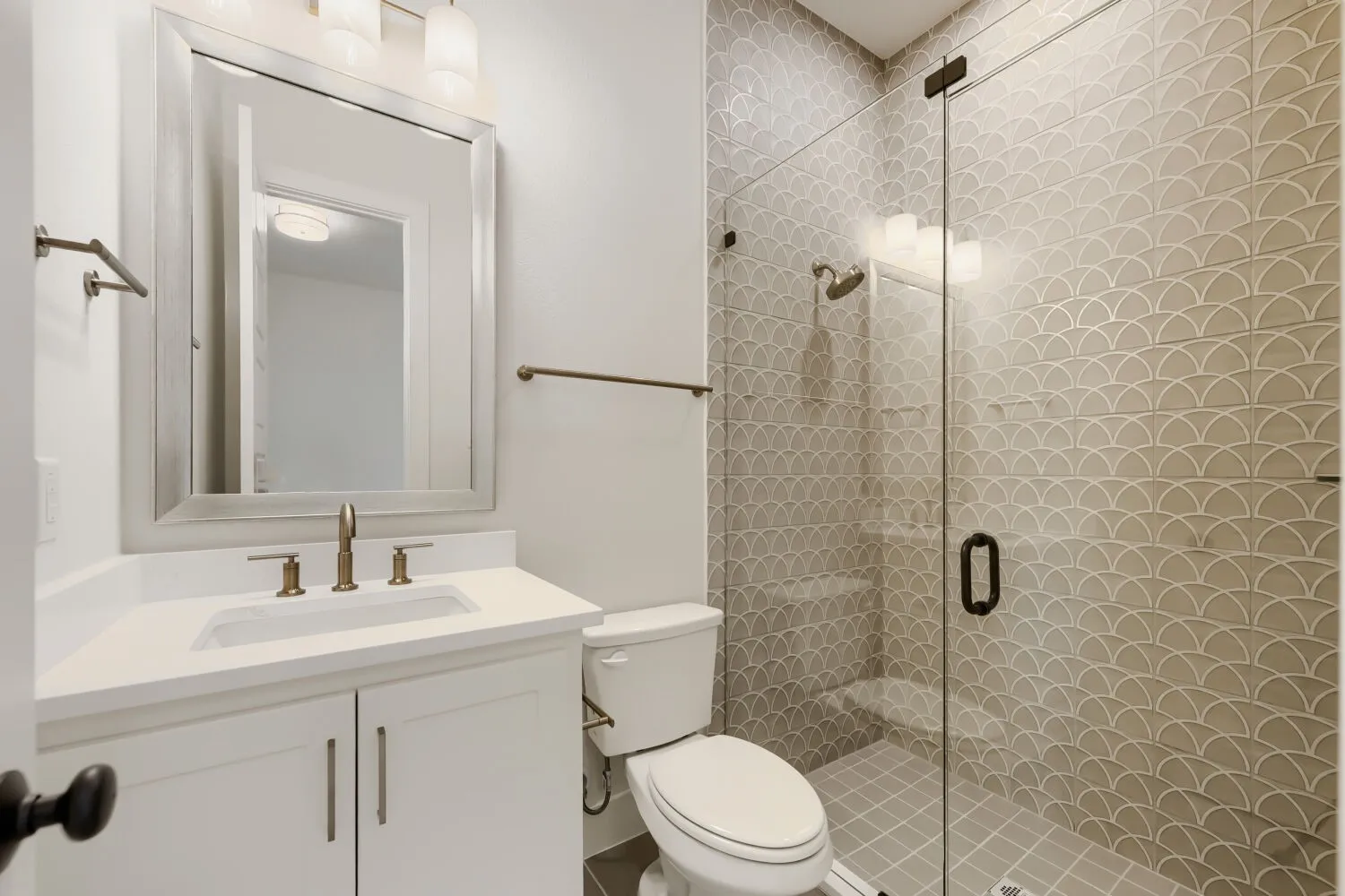 Bathroom featuring a glass-enclosed shower with decorative scallop tile, white vanity with integrated sink, and bronze-finish fixtures