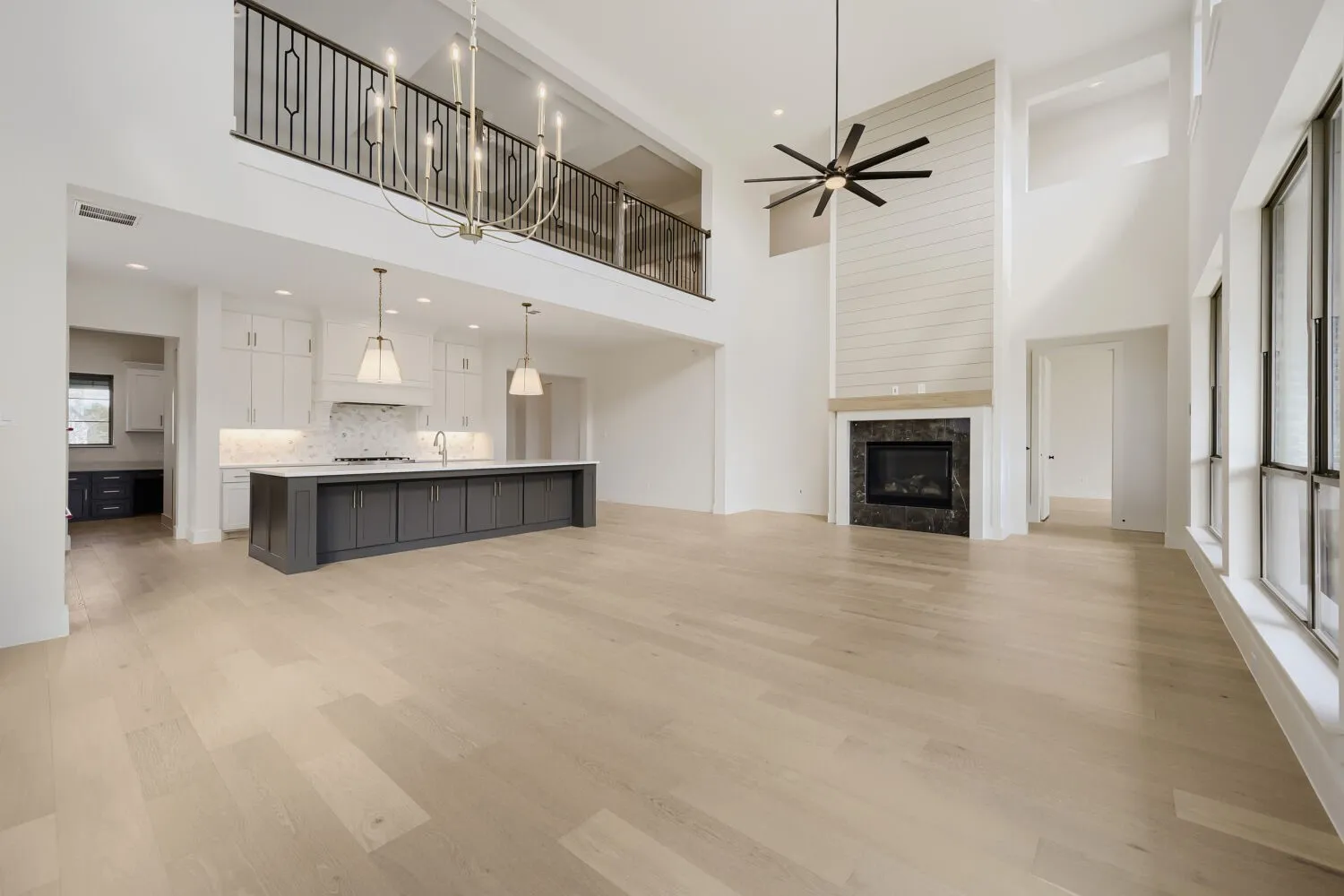 Two-story interior with wood-finish flooring, a kitchen island with seating, pendant lighting, and a fireplace with shiplap-paneled surround