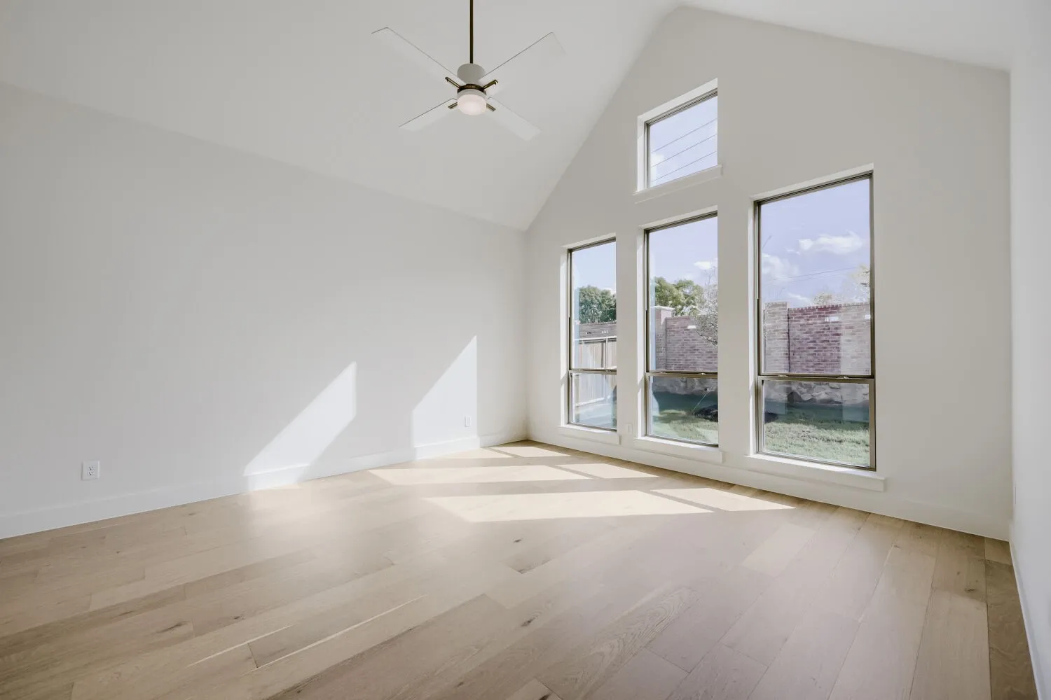 Vaulted ceiling, contemporary ceiling fan, light wood-finish flooring, and multiple windows