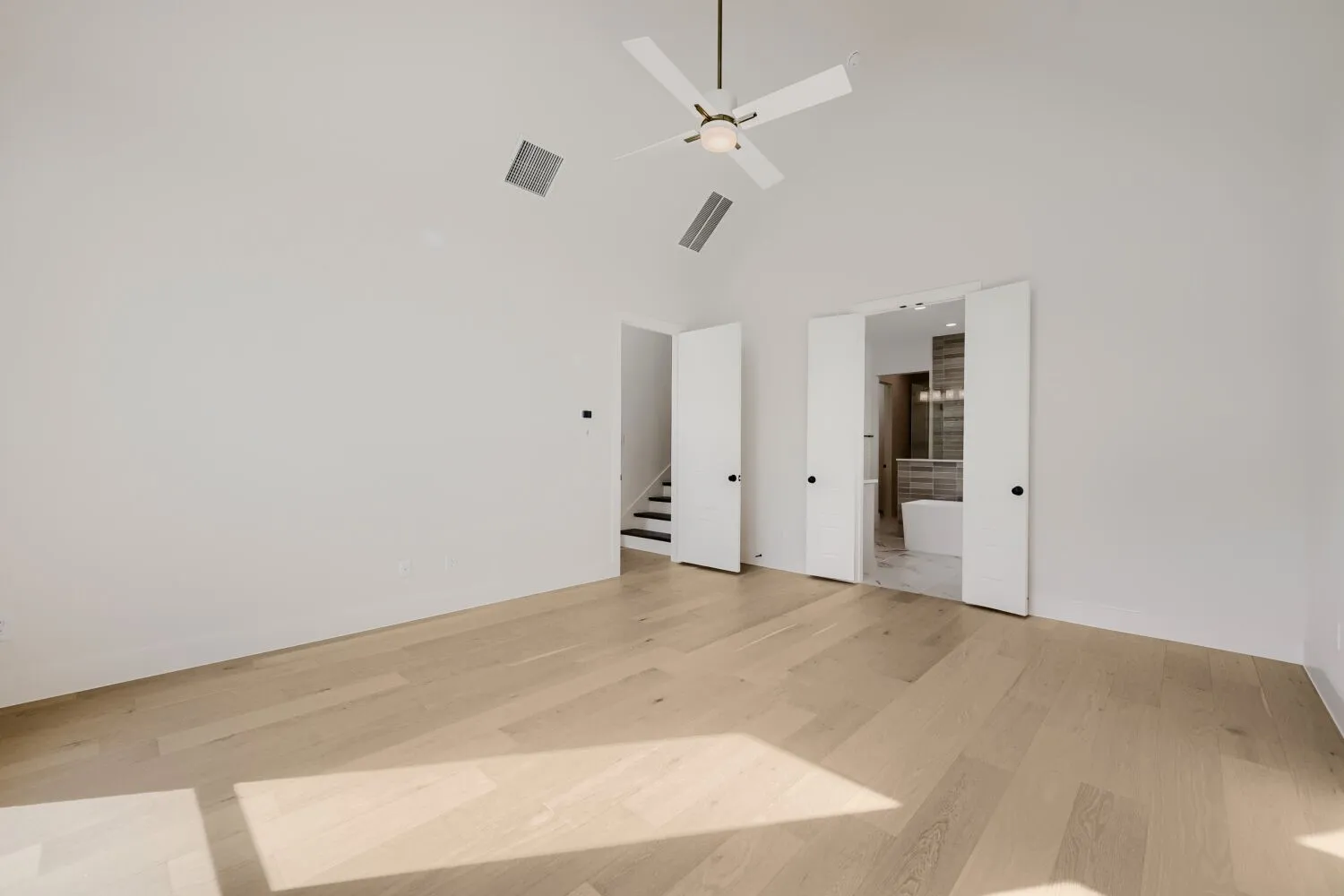 Vaulted ceiling with a ceiling fan, light wood-finish flooring, and white bifold doors revealing a freestanding bathtub
