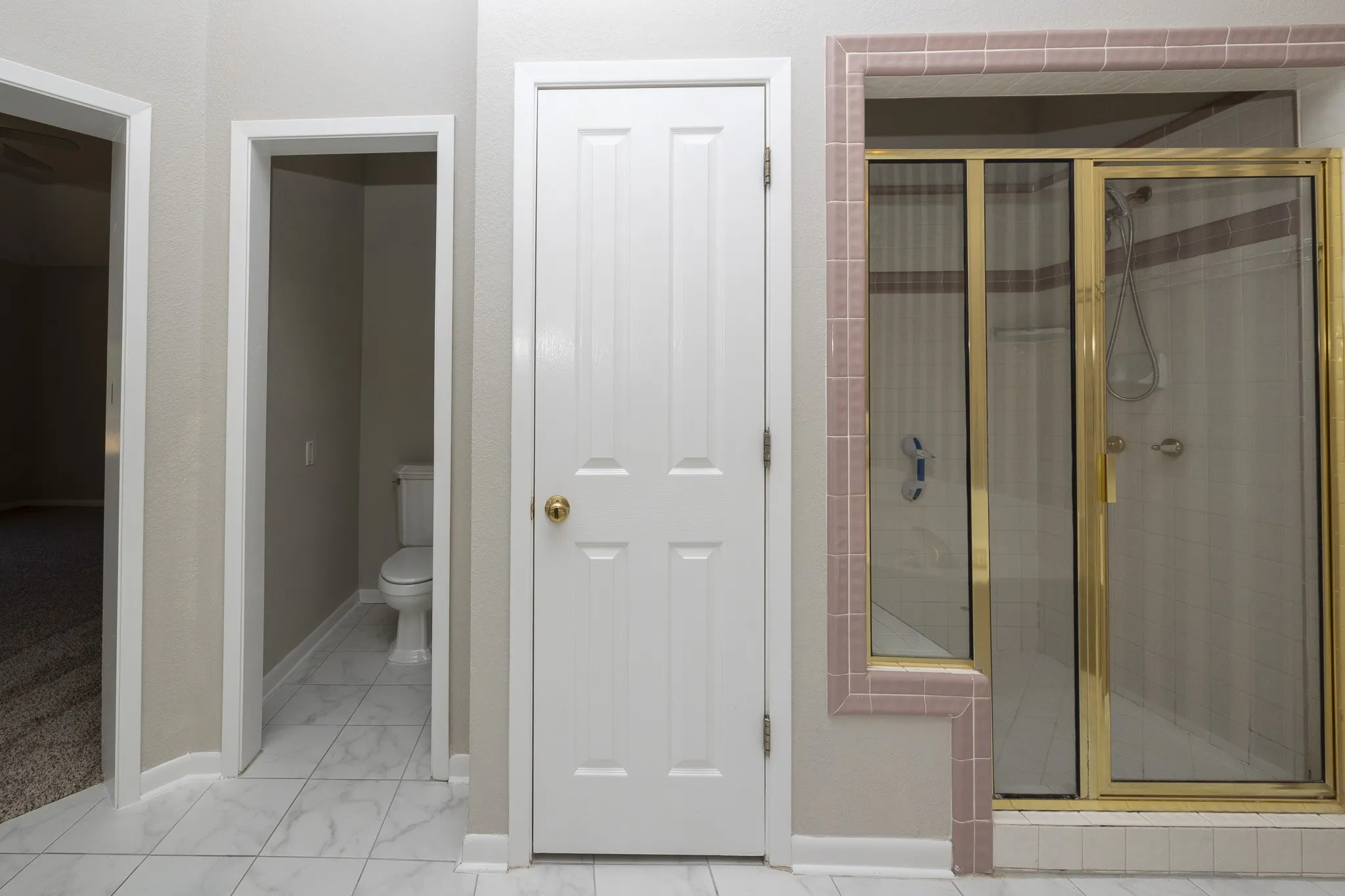 White large format tile flooring and a fully enclosed shower with brass-finish framing