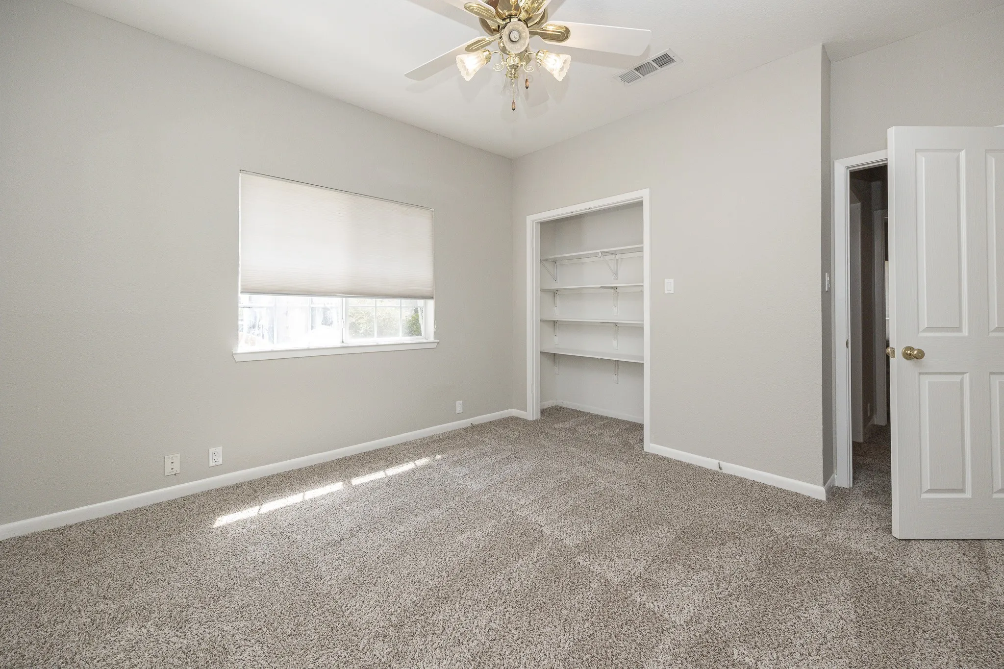 Carpeted flooring, built-in shelving, ceiling fan, window with roller shade, and paneled interior door