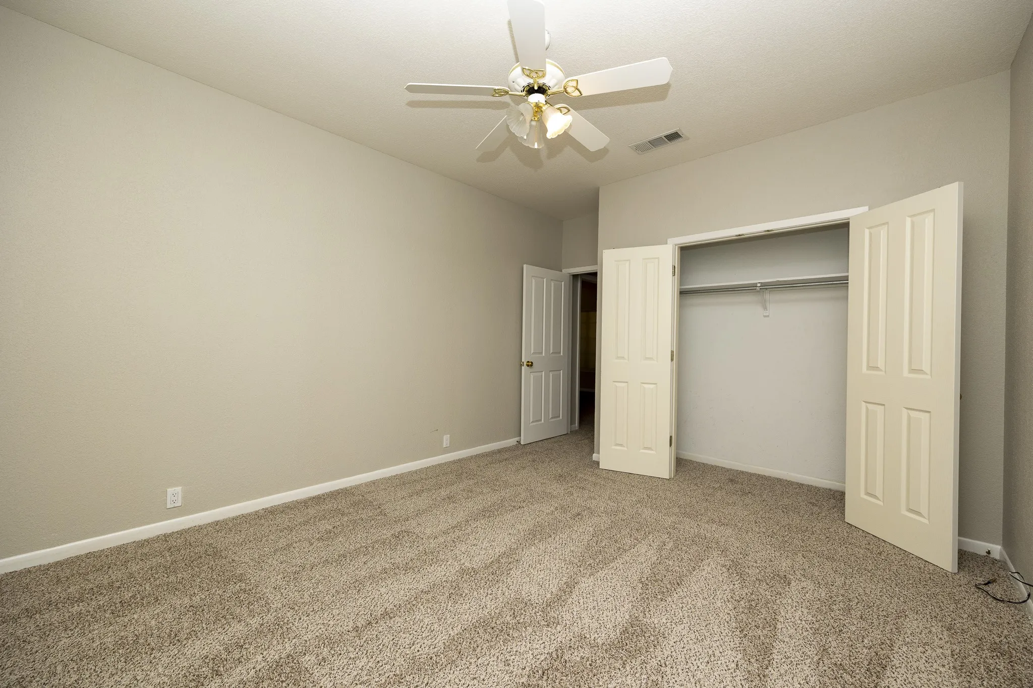 Neutral-toned carpeting, light-colored walls, ceiling fan with lighting, double bi-fold closet, and interior door