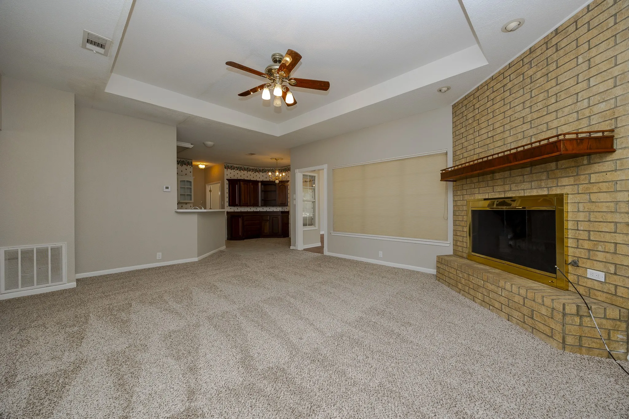 Recessed lighting, ceiling fan, tray ceiling, brick fireplace with brass surround, and wood mantle