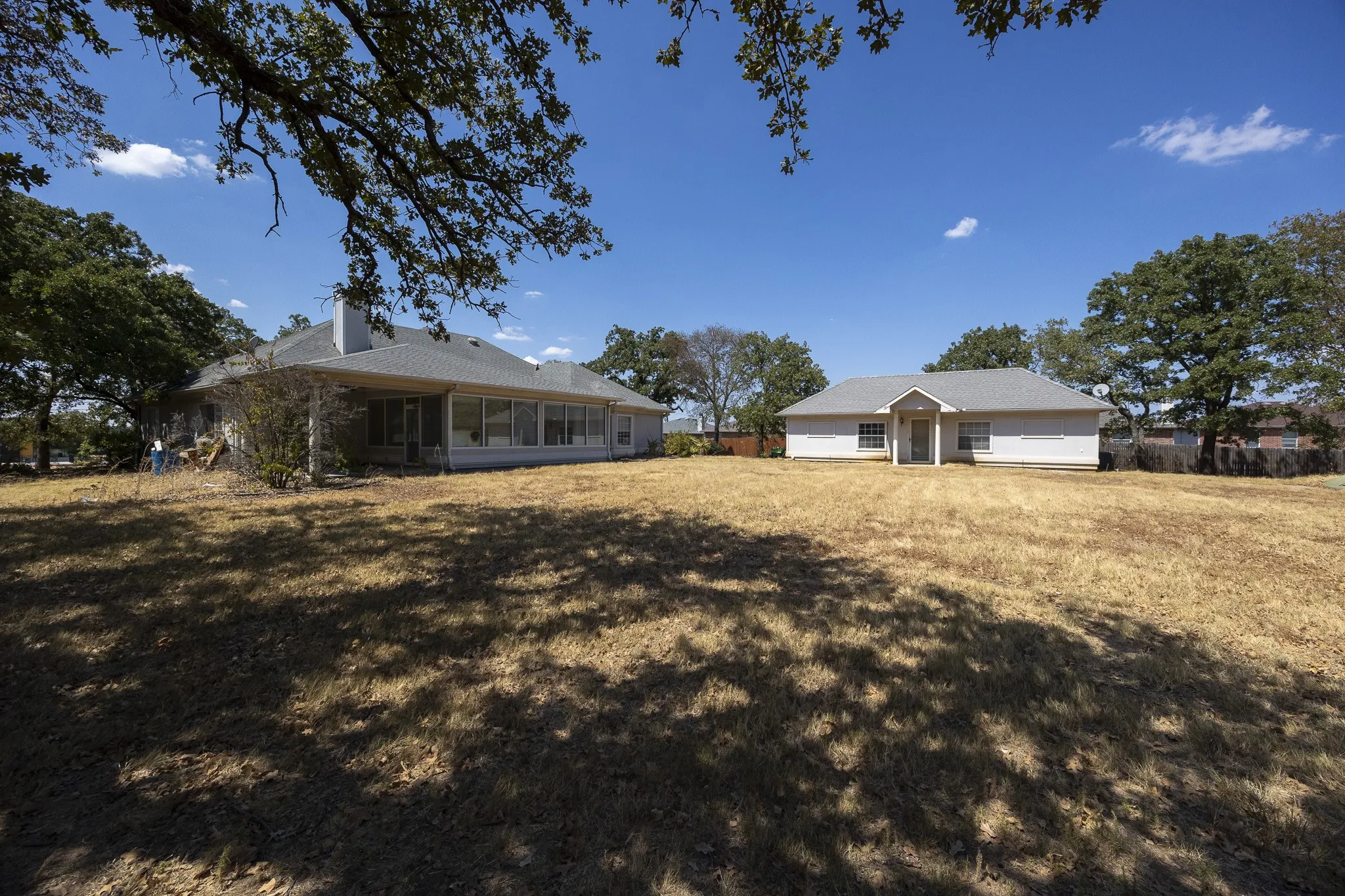 Expansive outdoor space featuring two separate structures, mature trees, and a substantial grassy area