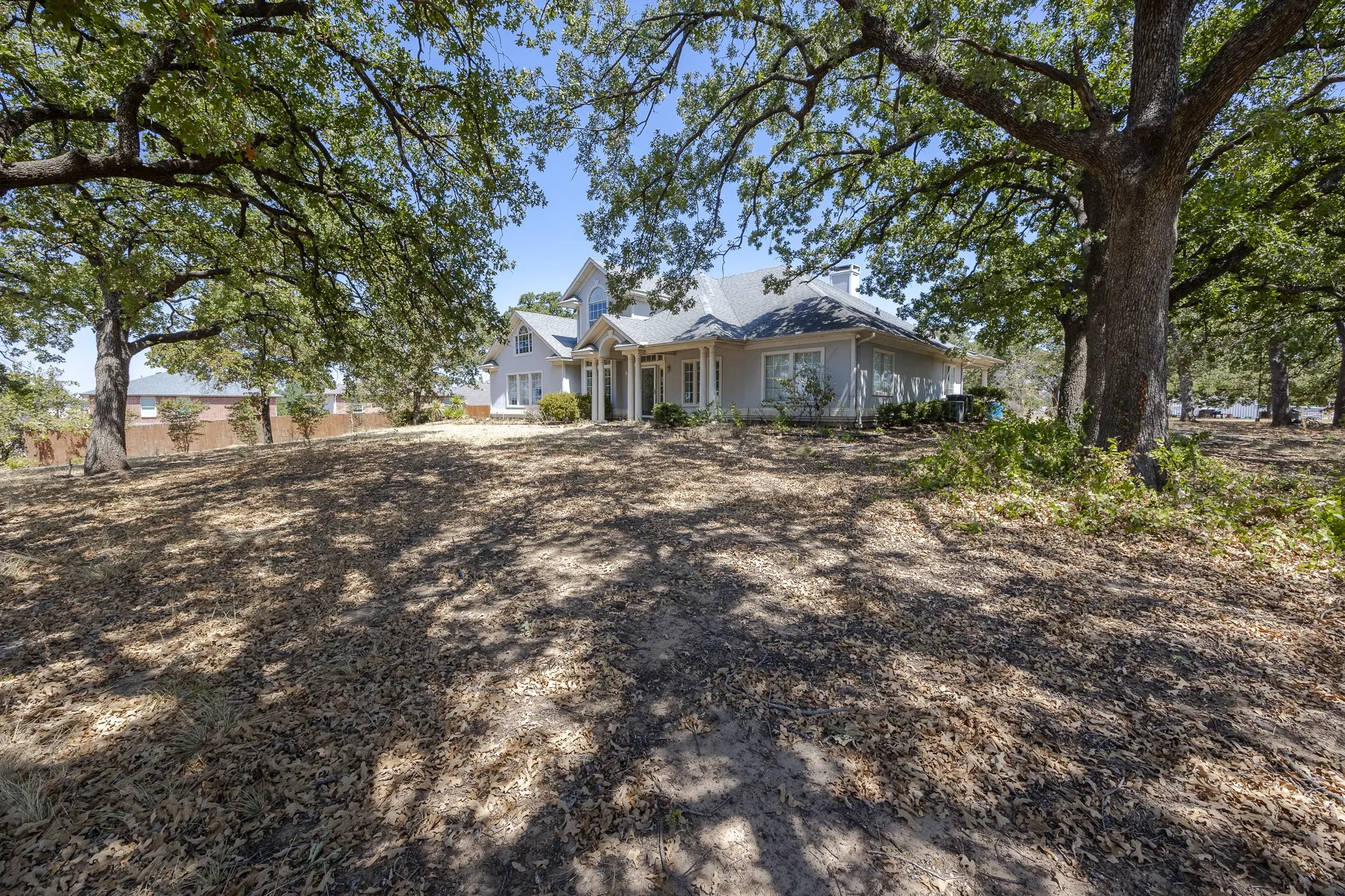 Expansive front yard with mature trees providing extensive canopy coverage, leading to a traditional-style residence with a prominent gabled roofline and multiple windows