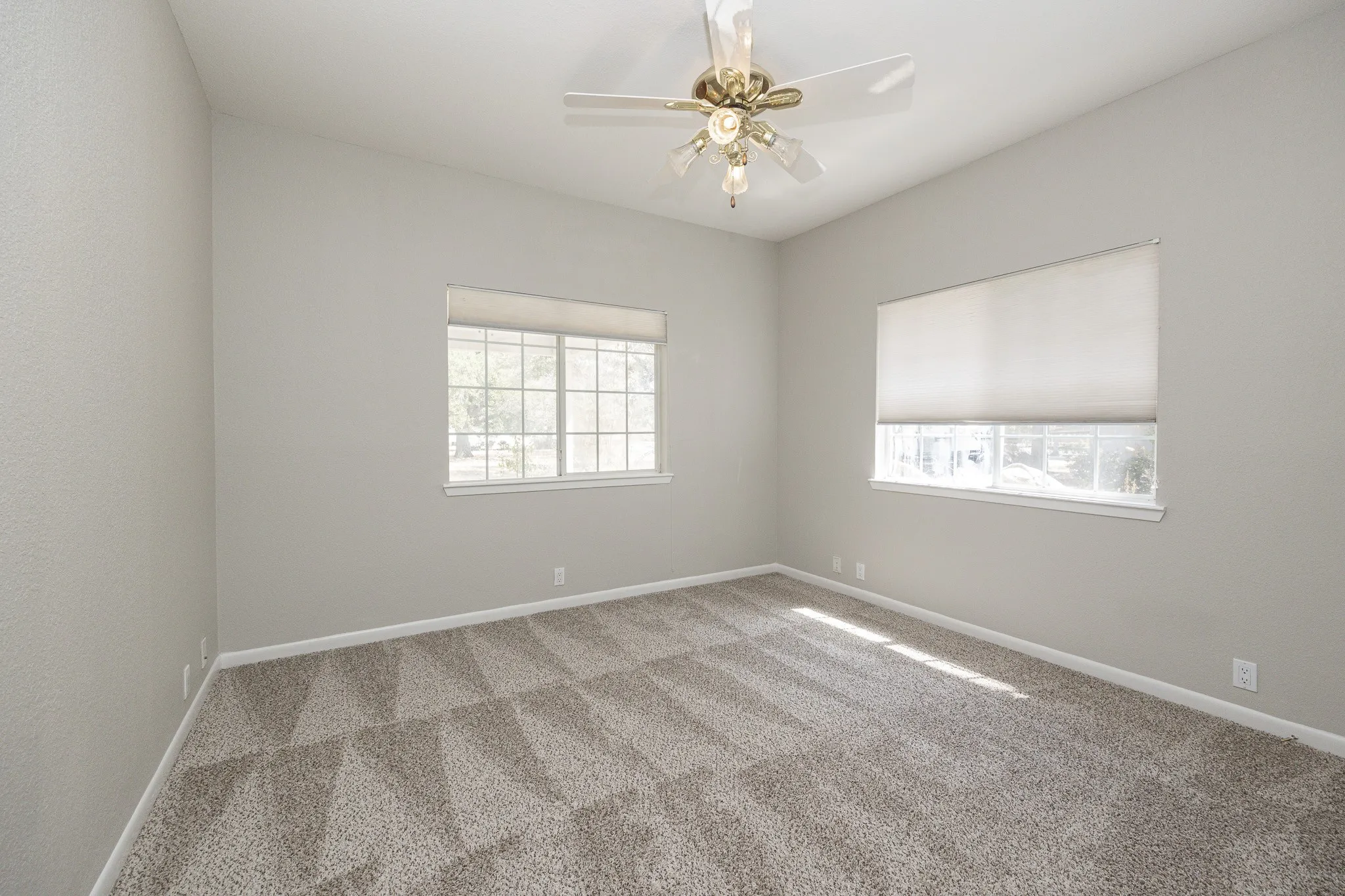 Vaulted ceiling, two windows with roller shades, ceiling fan with light fixture, and carpeted flooring