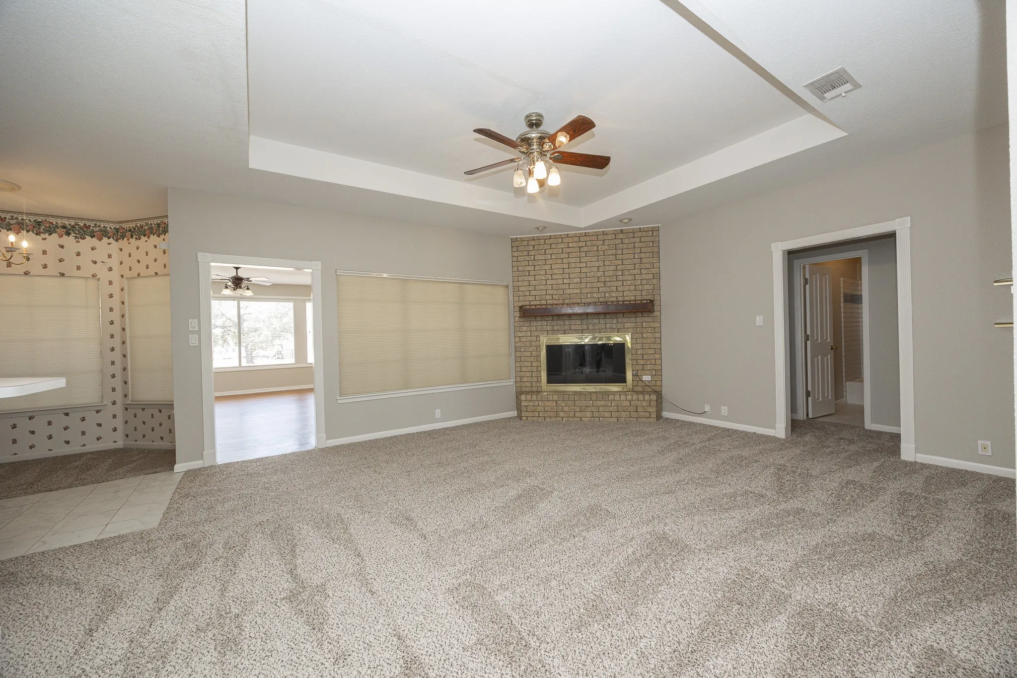 Tray ceiling with an attached ceiling fan, brick fireplace with a wood mantle, and light gray wall paint