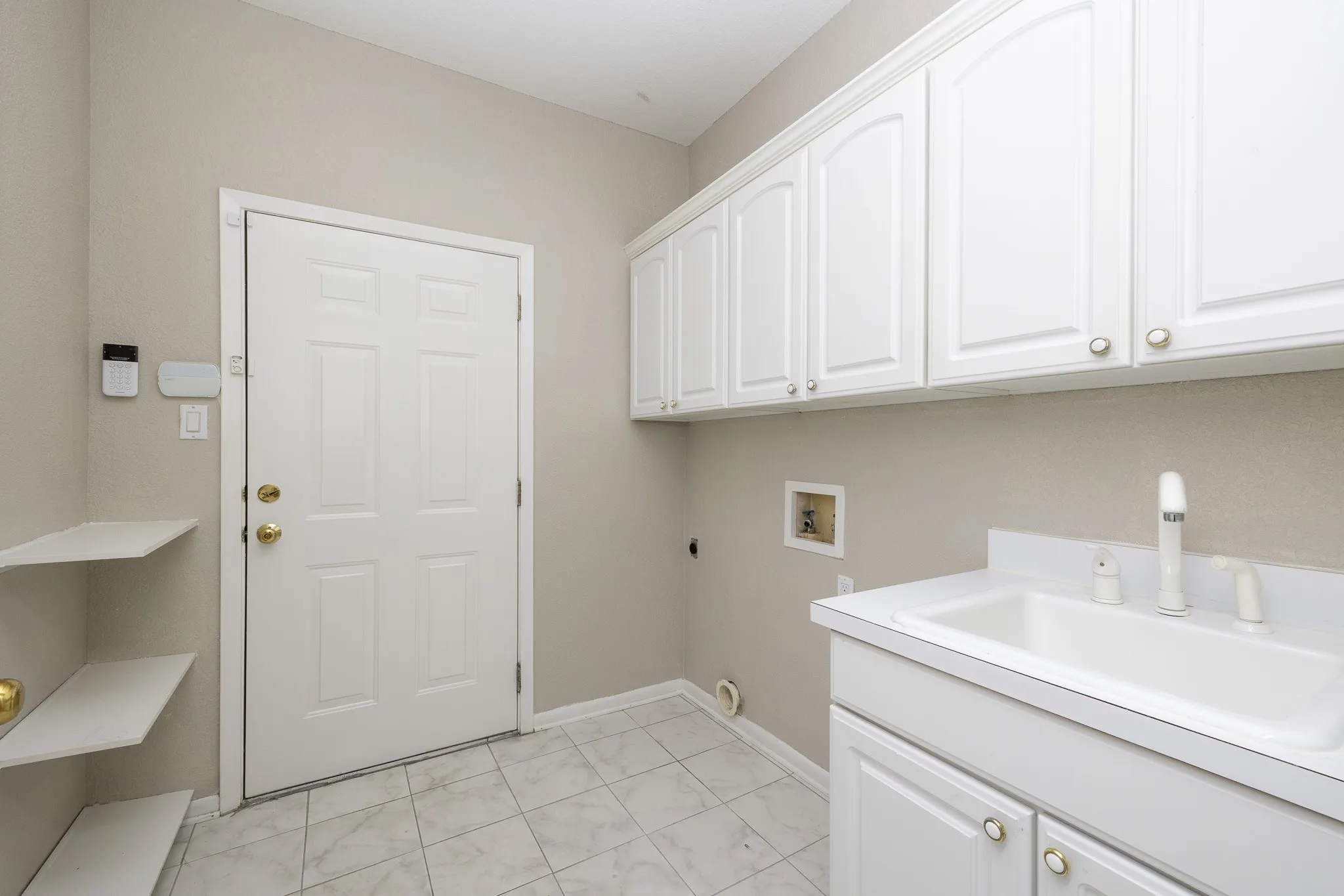 Laundry area featuring white cabinetry, a utility sink, wall-mounted shelving, and tile flooring