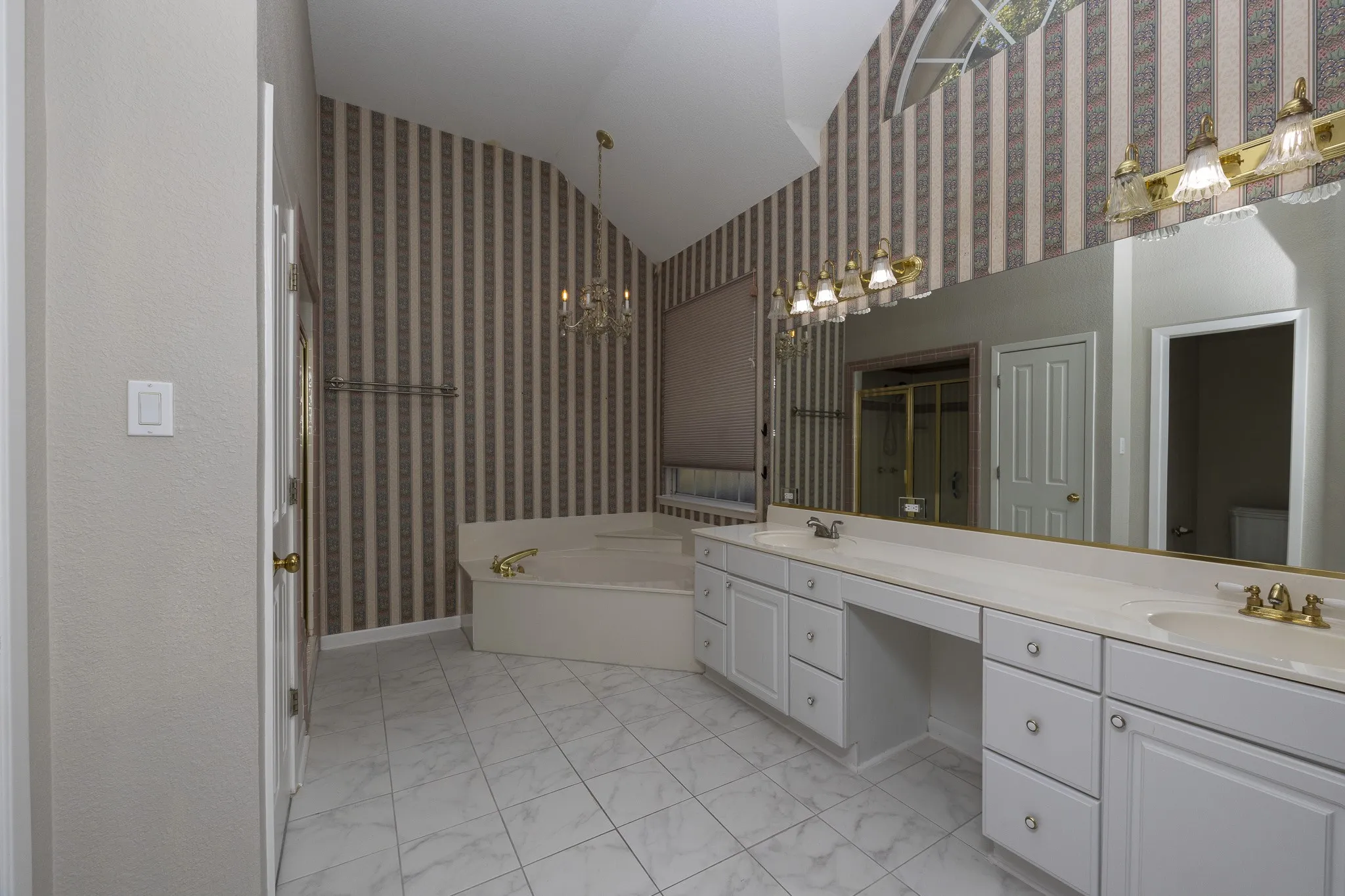 Vaulted ceiling, arched window, built-in soaking tub, extensive vanity with dual sinks, and tile flooring