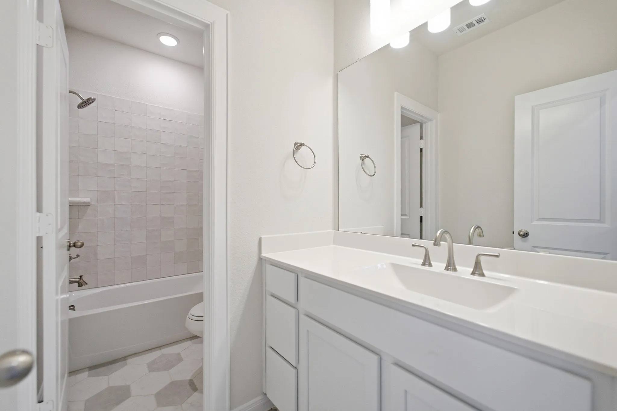 Bathroom featuring a white vanity with an integrated sink, brushed nickel faucet, large mirror, and overhead vanity lighting