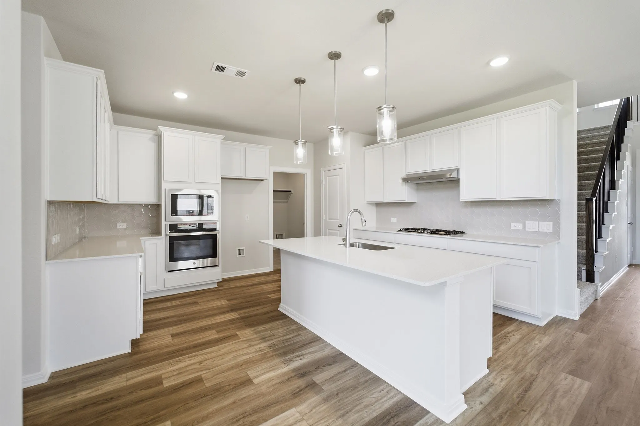 Modern kitchen featuring a large central island, white cabinetry, integrated stainless steel appliances, wood-finish flooring, and pendant lighting
