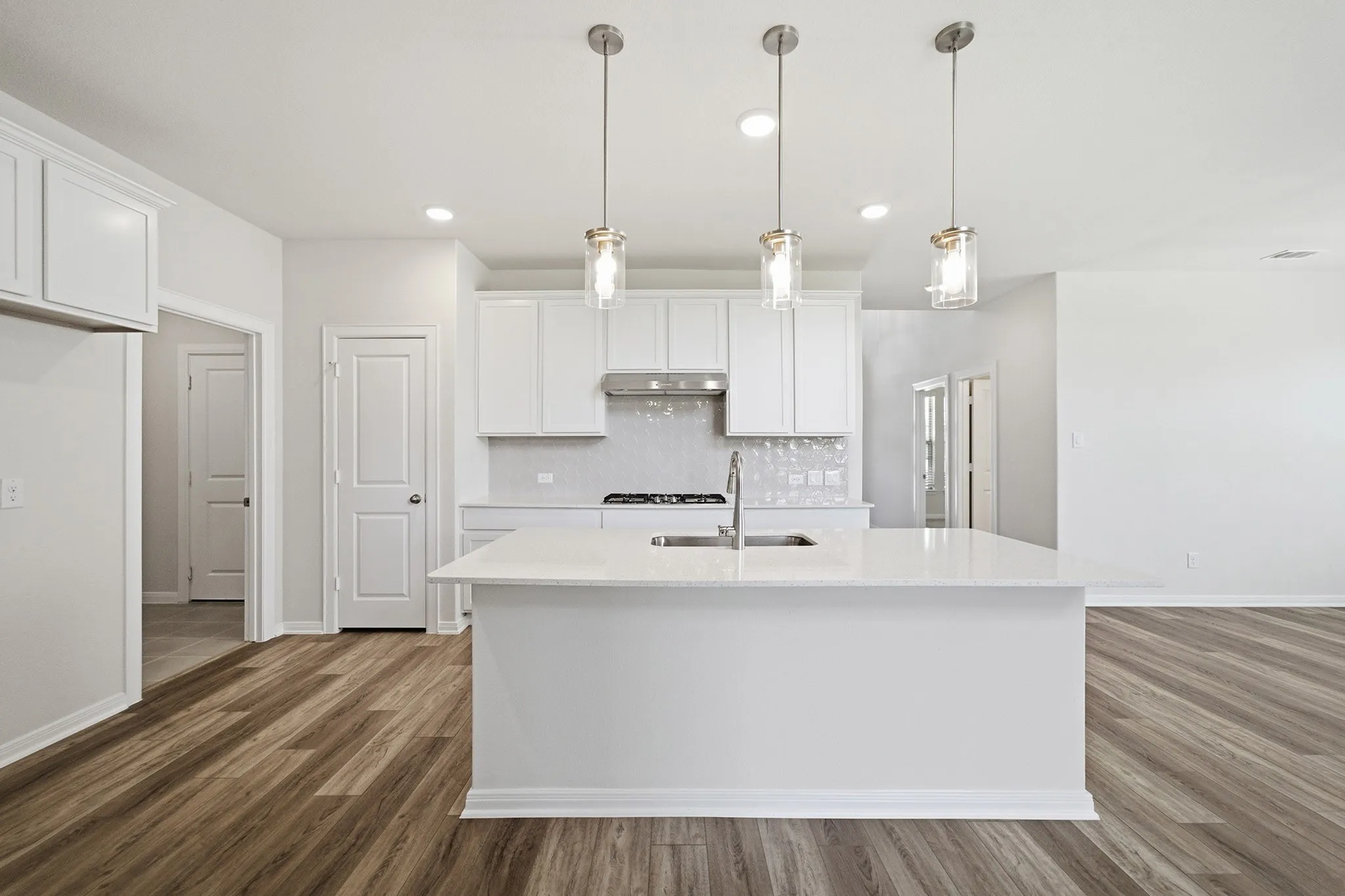 Modern kitchen featuring a large center island with a stainless steel sink and faucet, white cabinetry, a light-toned tile backsplash, and wood-finish flooring