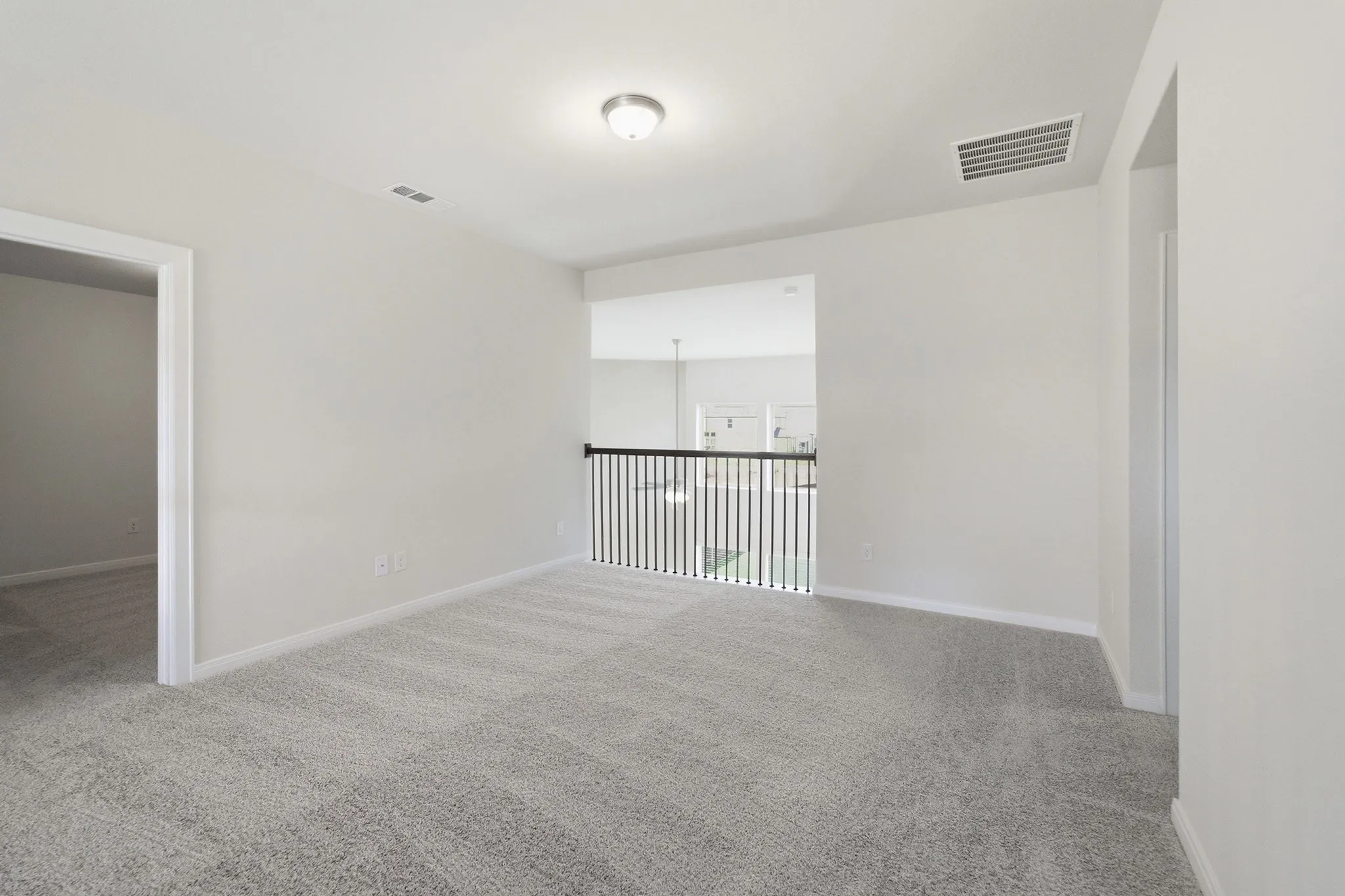Open loft space featuring light gray textured carpeting, neutral wall paint, and a black wrought iron railing overlooking a lower level